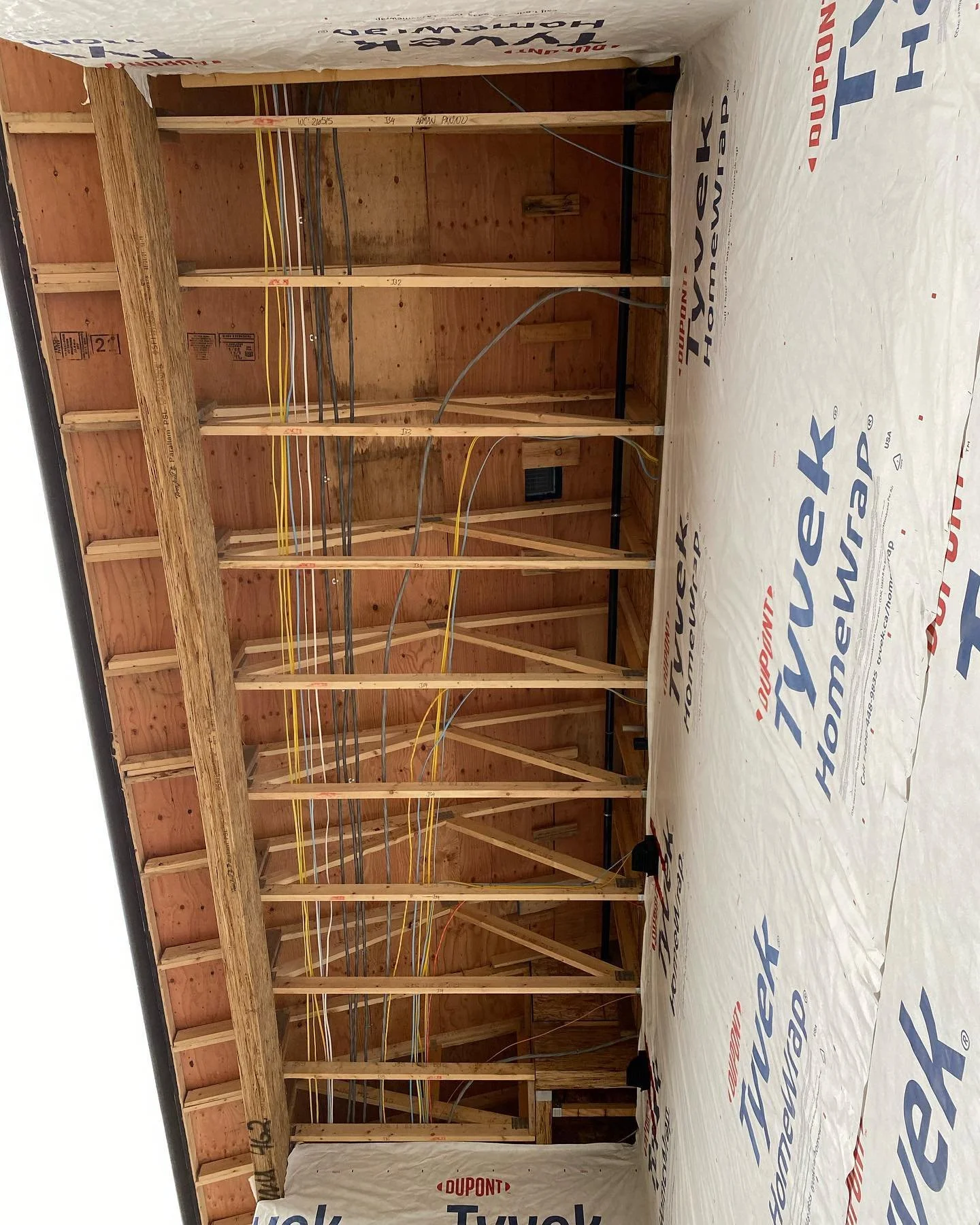 Under construction interior with exposed wooden studs, electrical wiring, and a sheet of insulation labeled 'DuPont Tyvek,' on a concrete floor.