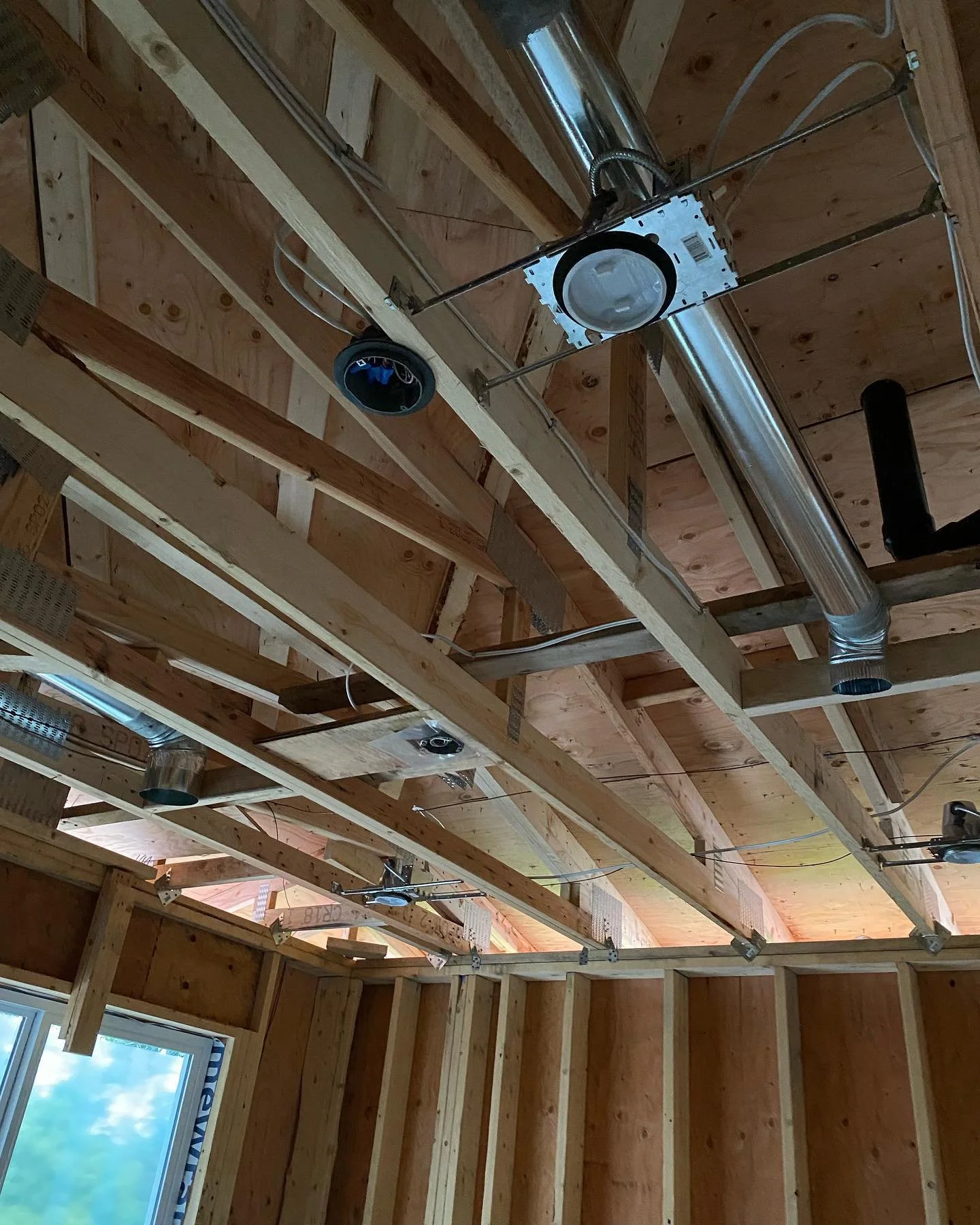 Construction site ceiling with exposed wooden beams, electrical wiring, ductwork, and recessed lighting fixtures.