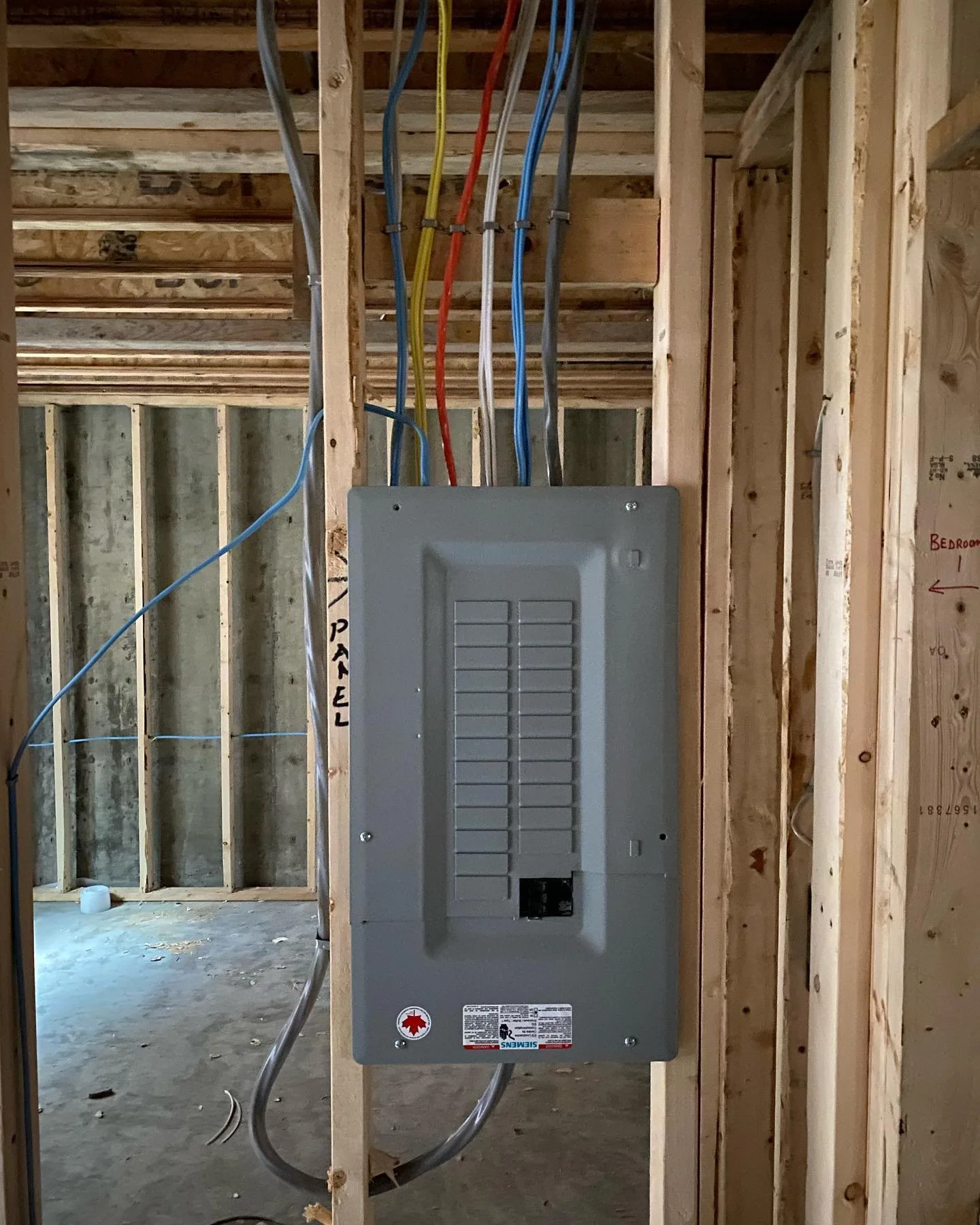 Electrical panel installed between wooden studs in a construction site.