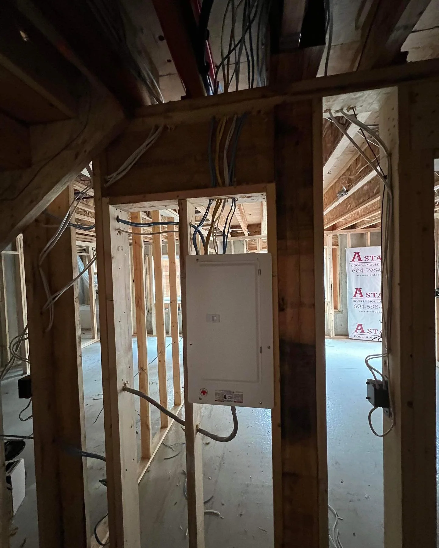 Interior view of a building under construction with exposed wooden framing, electrical wiring, and a visible electrical panel.