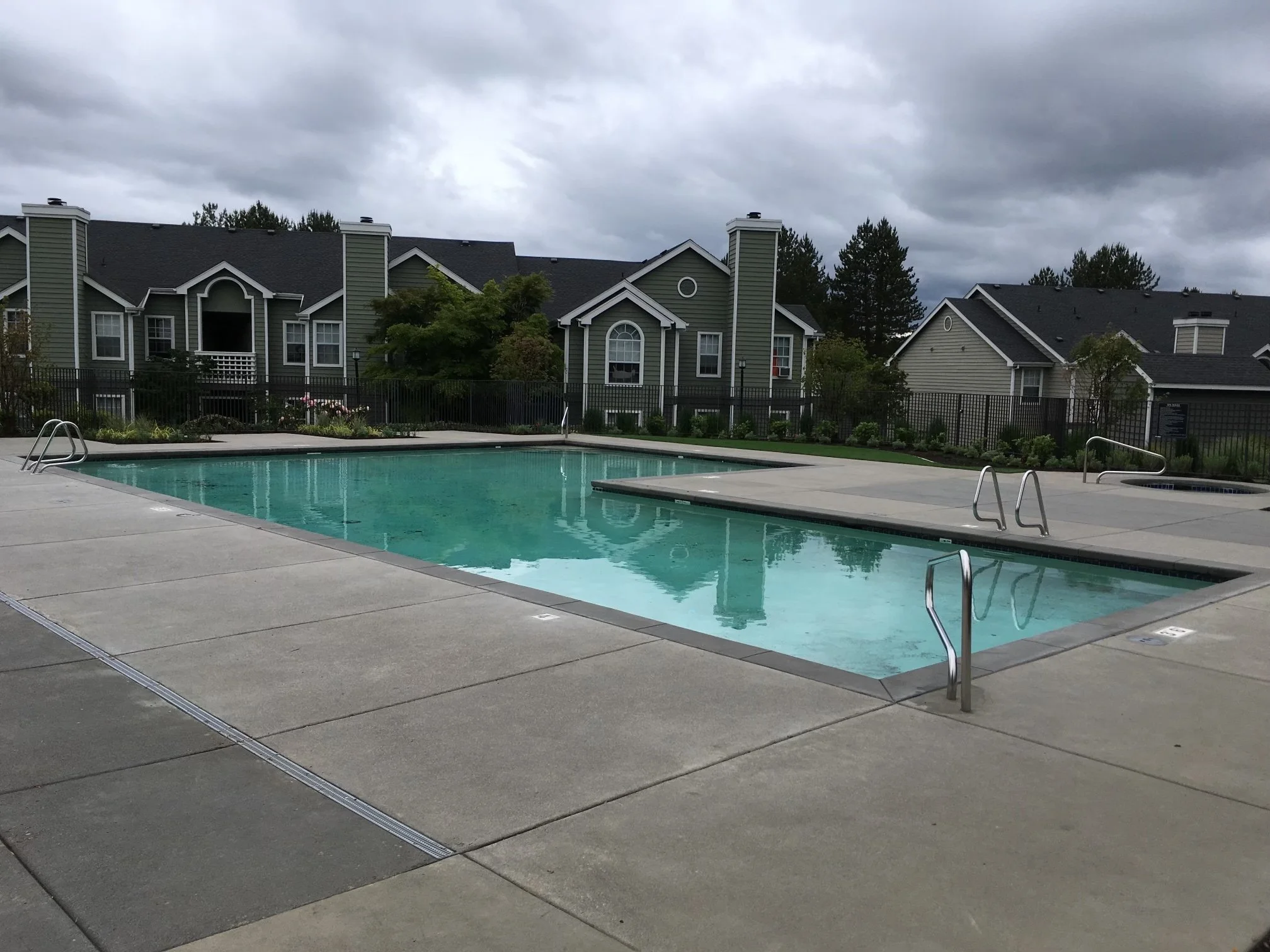 A swimming pool in an apartment complex in Happy Valley, ORegon with residential buildings and trees in the background under a cloudy sky.