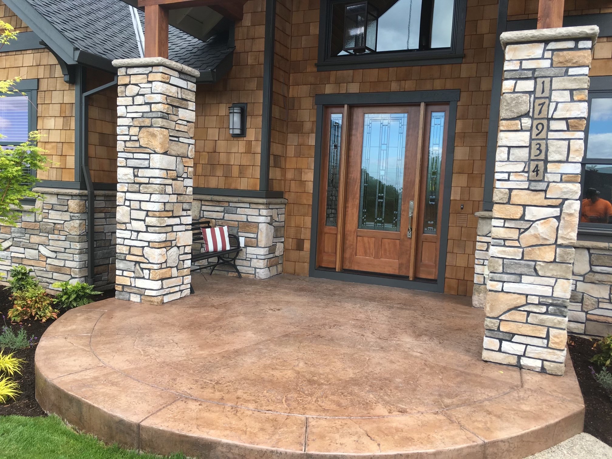 Front porch of a house with stone pillars, a wooden door, and a concrete porch in a landscaped yard of Portland, Oregon
