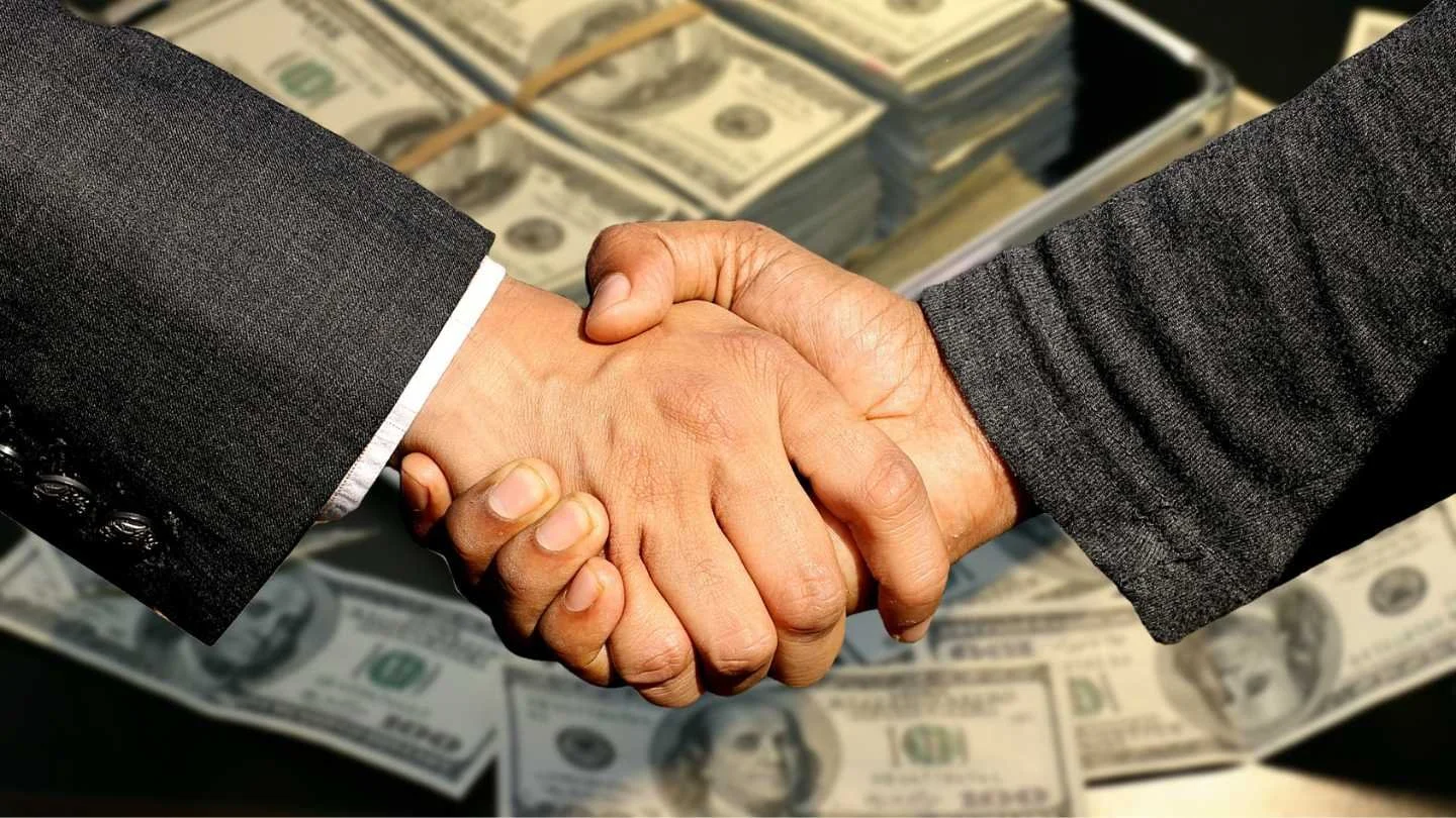 two men shaking hands in front of cash