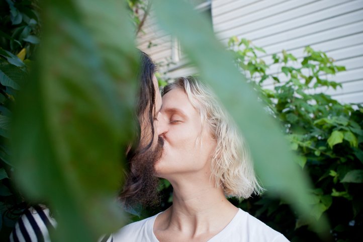 Randy &amp; Kelsey Taylor kiss in their backyard with a leaf in the foreground at their home in Hudson, NY