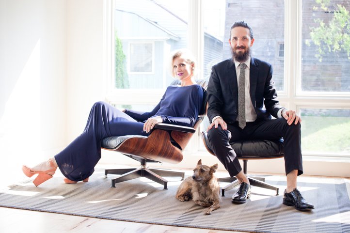 Randy & Kelsey Taylor sit in office chairs with their dog at their feet in their home in Hudson, NY