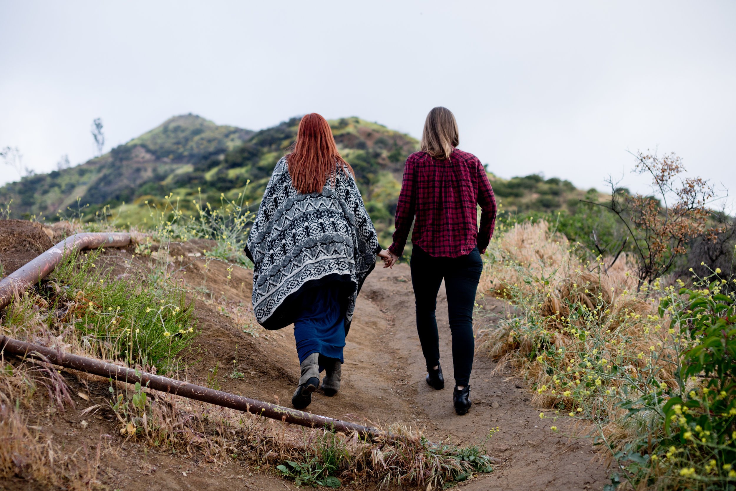 Courtney &amp; Tierney walking up a hiking trail away with their backs to the camera, holding hands