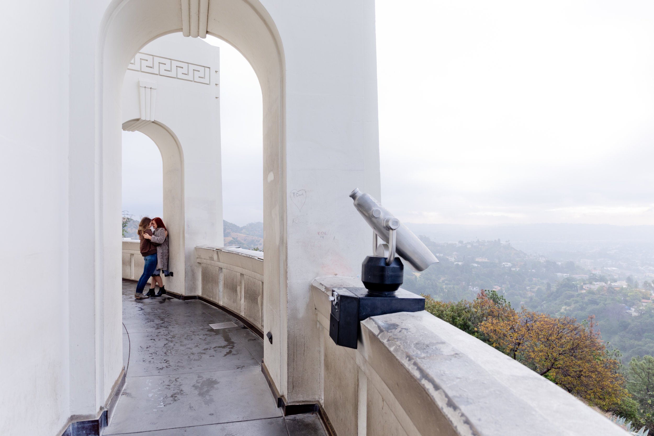 Long shot of Grace &amp; Tierney kissing under an arch at Griffith observatory in LA with a tower viewer in the foreground