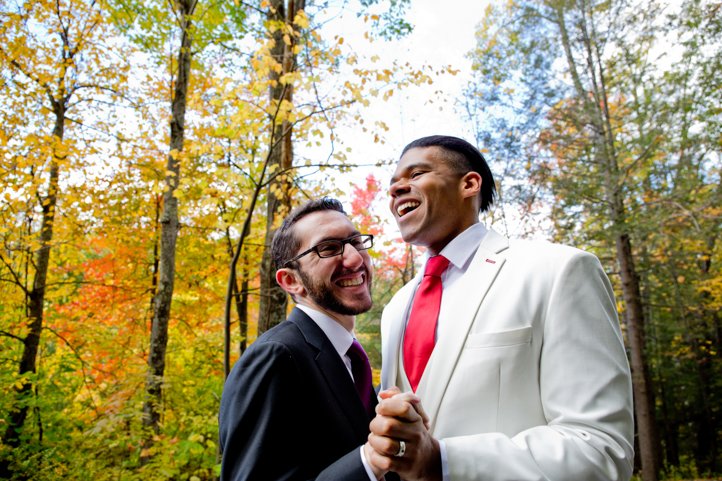 Arthur &amp; Scott smile holding hands in front of fall foliage in the Catskills