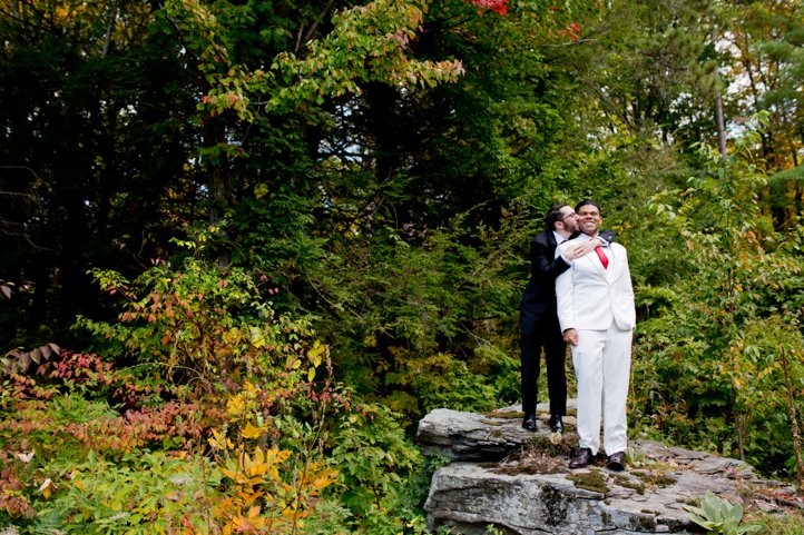 Arthur and Scott embrace on top of a rock with fall foliage in the background in Hudson Valley NY