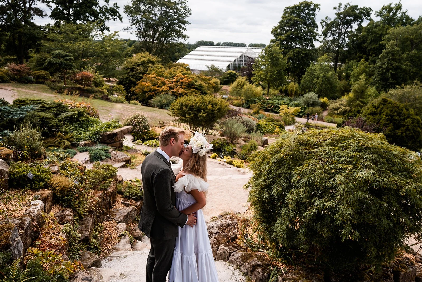 A couple dressed in wedding attire sharing a kiss in a lush garden.