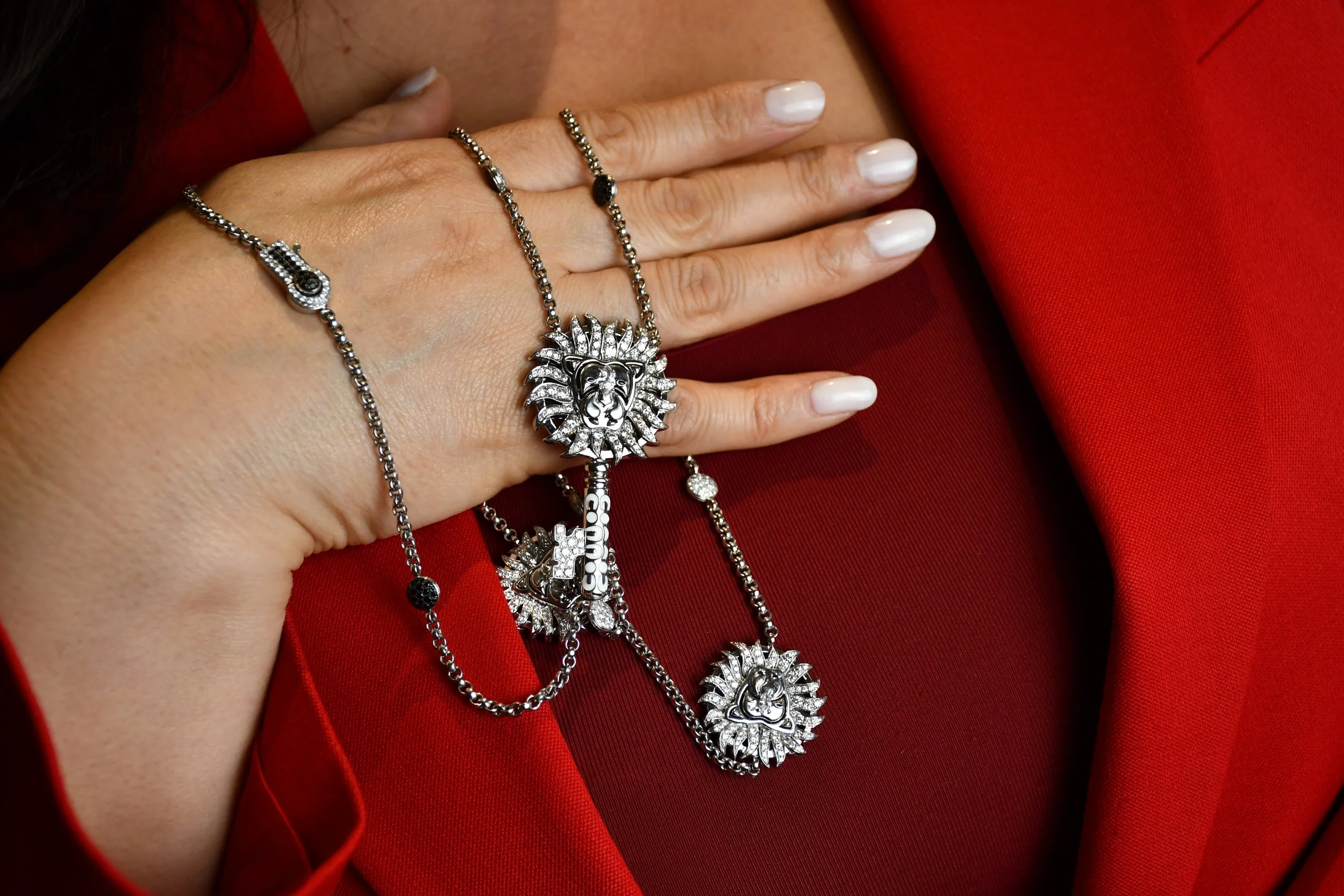 A woman's hand with rings, resting on a red garment, adorned with silver chains and jewelry. Mathon ParisHigh jewellery 