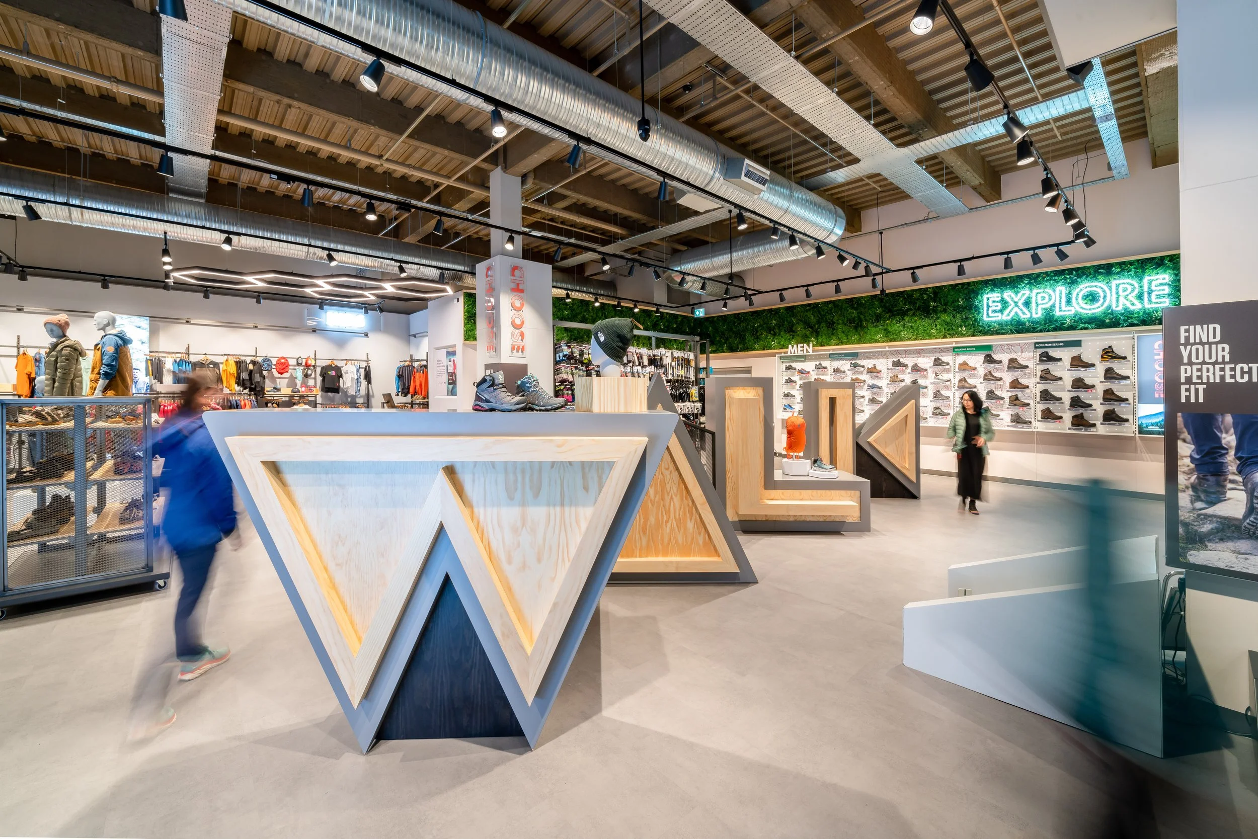 Entrance to a retail store with clothing and outdoor gear, featuring a wood-paneled facade and a digital display on the left side.