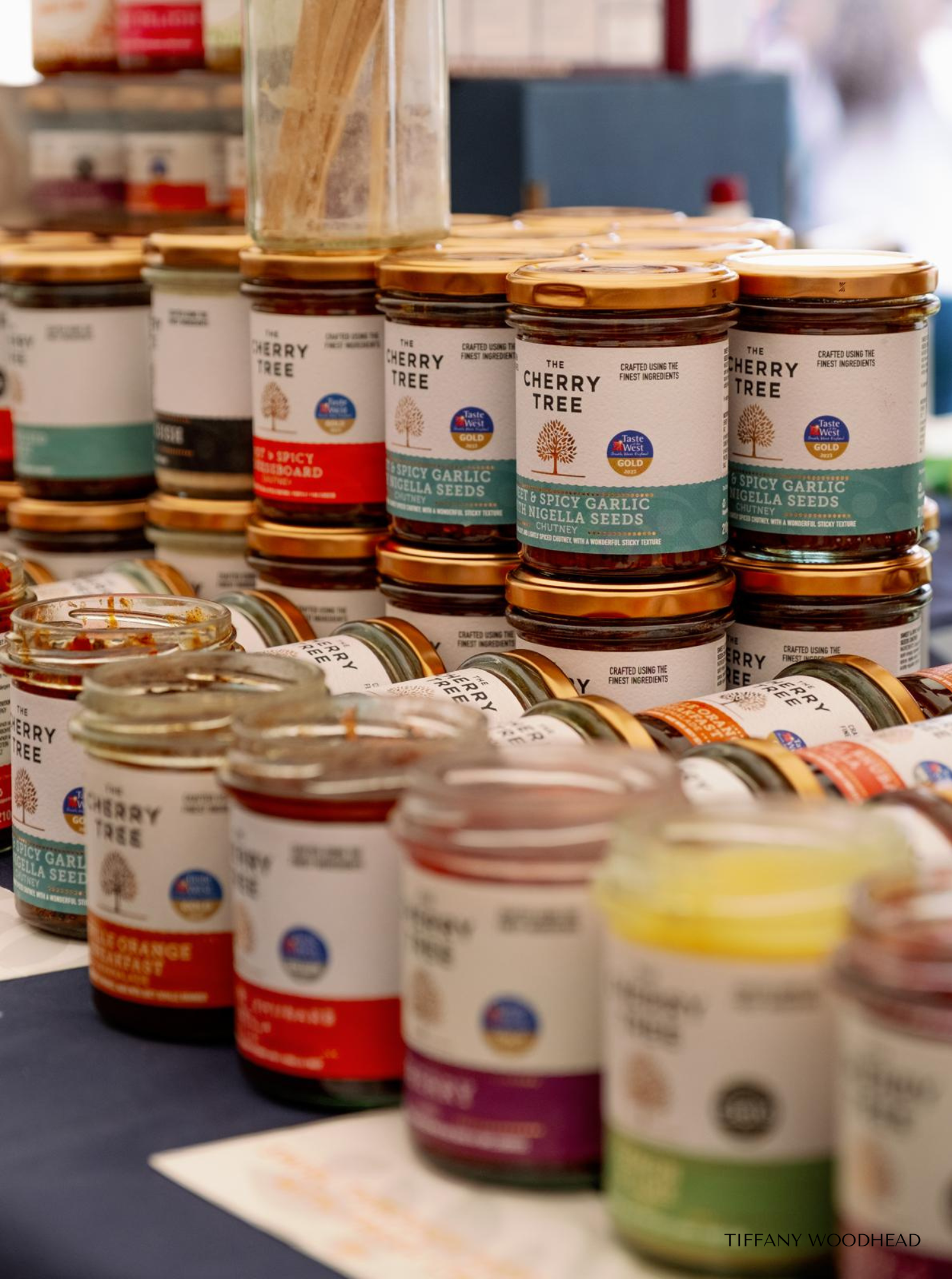 Display of various jars of Cherry Tree brand spreads and chutneys on a store shelf with gold and green lids.