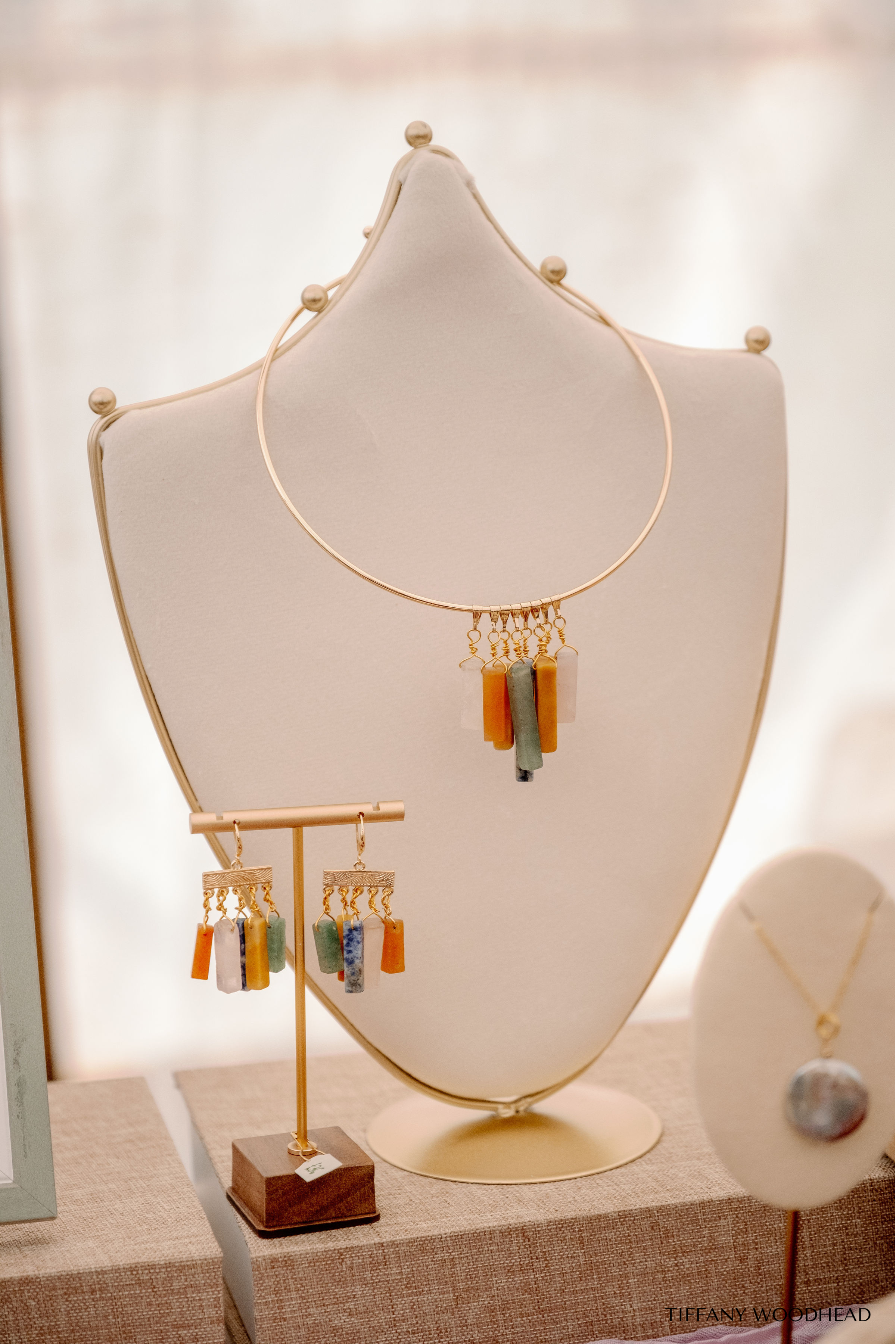A display of colorful handmade earrings on a jewelry stand, with a necklace hanging on the same stand, all arranged on a table at a boutique or gallery.