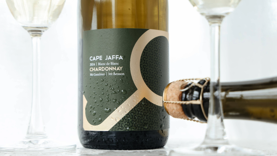 A hand holding a swirling glass of white wine mid-splash, with bright coastal light and sea spray in the background — capturing the carefree, coastal spirit of Cape Jaffa Wines’ Crew Mates Wine Club.