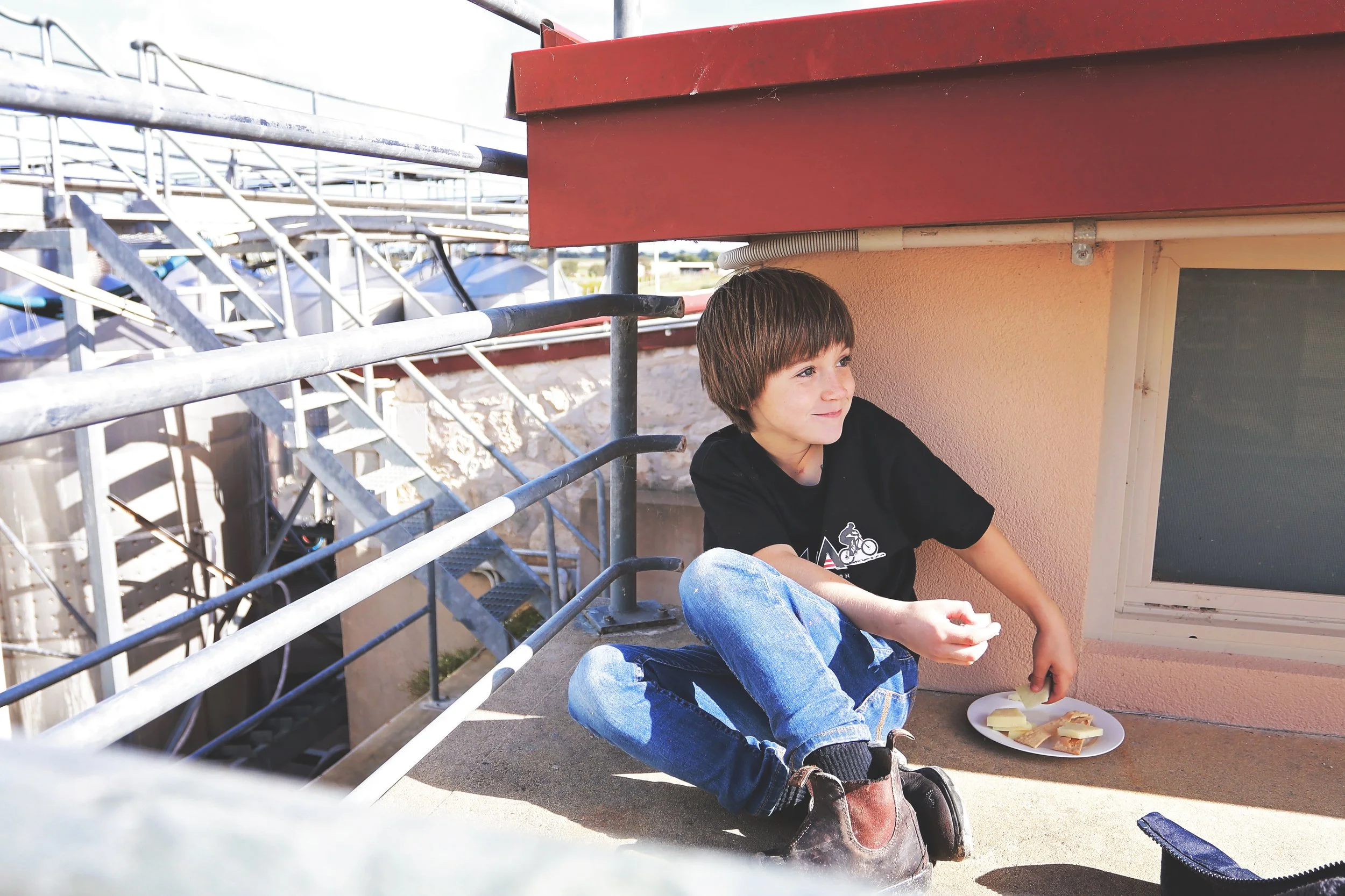Charlie Hooper sitting on the winery ledge mid-snack at Cape Jaffa Wines; growing up among tanks, vines, and salty sea breezes.
