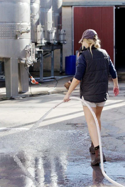Daisy Hooper hosing down the winery pad at Cape Jaffa Wines; part of the Hooper family behind this hands-on, biodynamic coastal vineyard in South Australia.