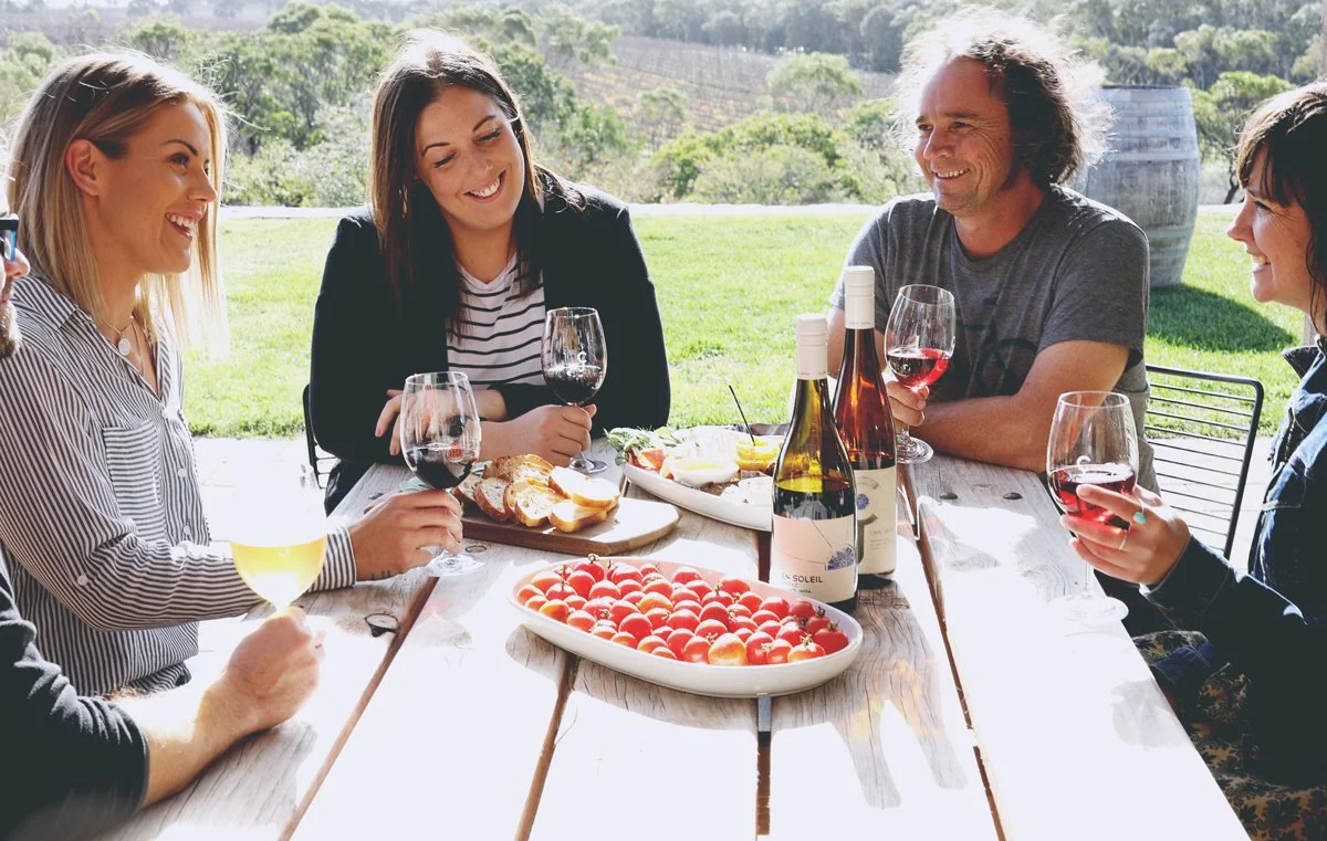 Guests enjoying wine, a cheese grazing platter, and the sun; during a Cape Jaffa Wines event — casual vibes with live music and coastal wine.