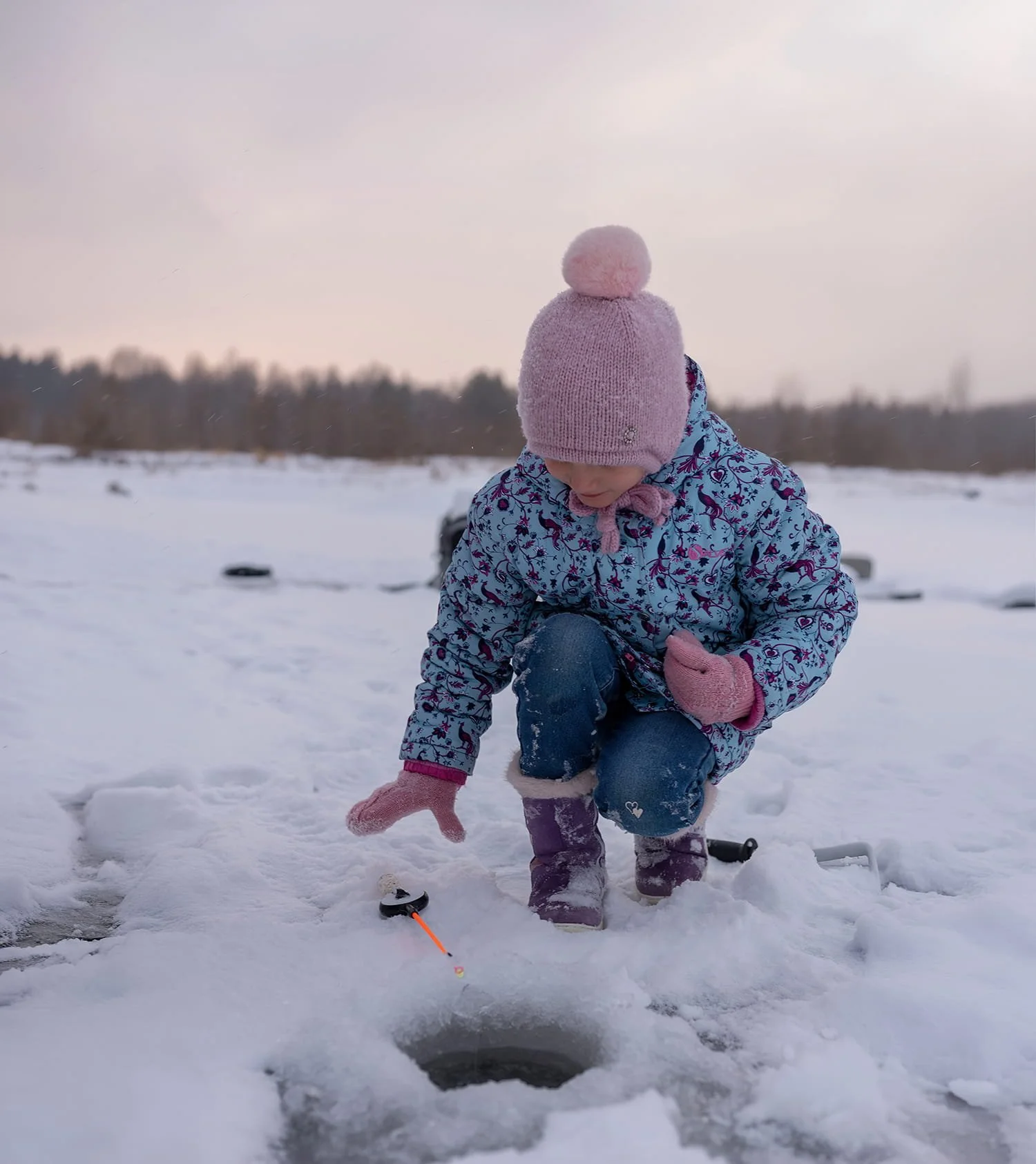 Young girl in winter clothing ice fishing on a frozen lake during daytime.