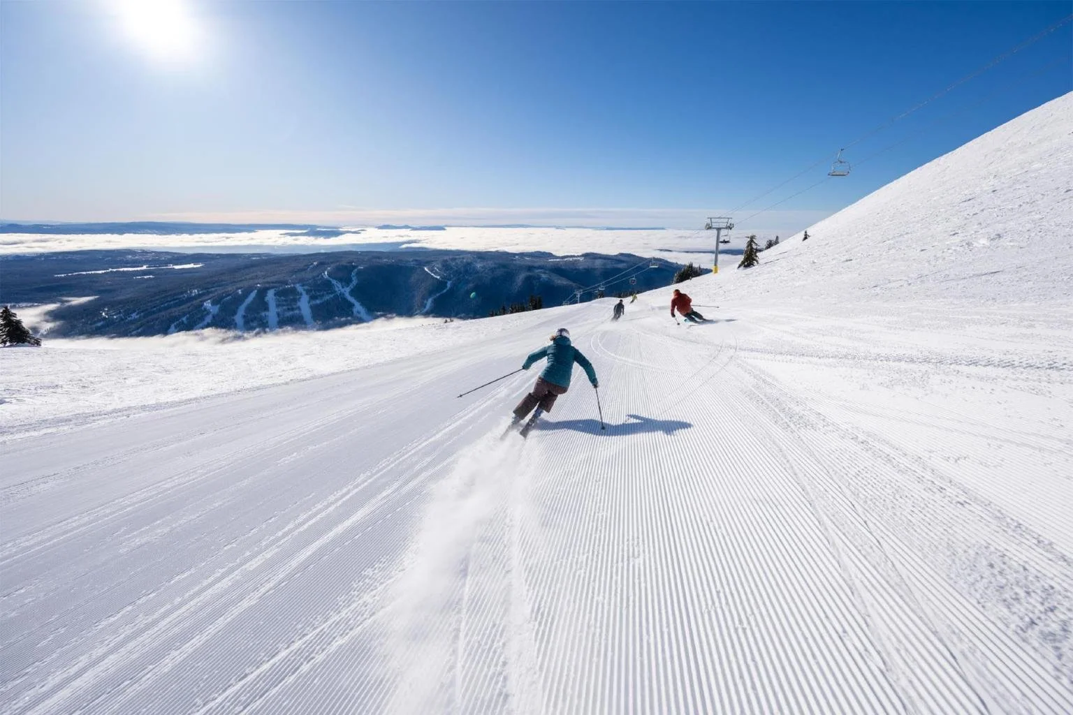 Skier descending a snow-covered slope under a clear blue sky at a ski resort.