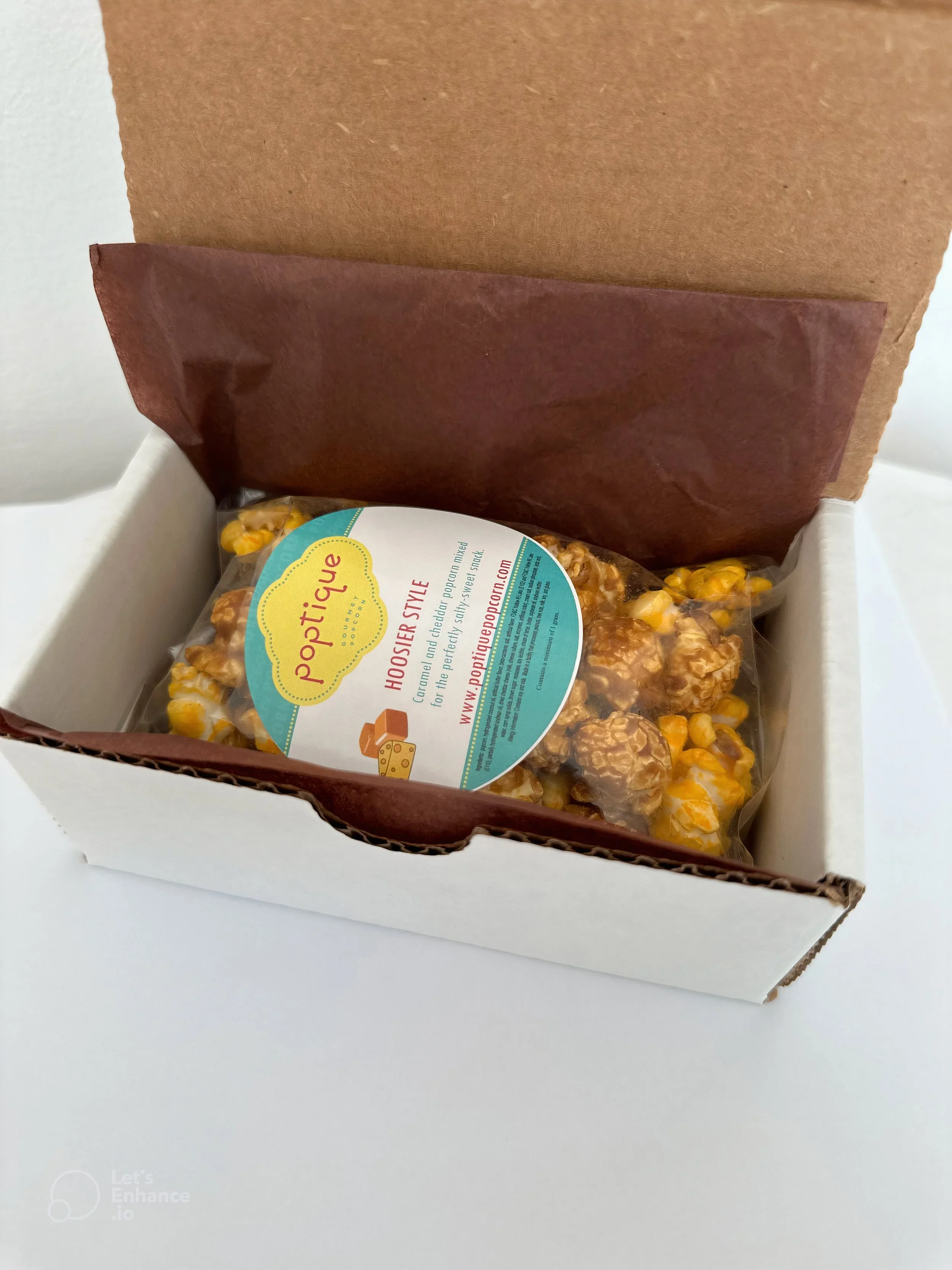 A box with popcorn inside, labeled 'PopTwig' and 'Horseshoe Style,' with a description about caramel-coated popcorn, on a white surface.