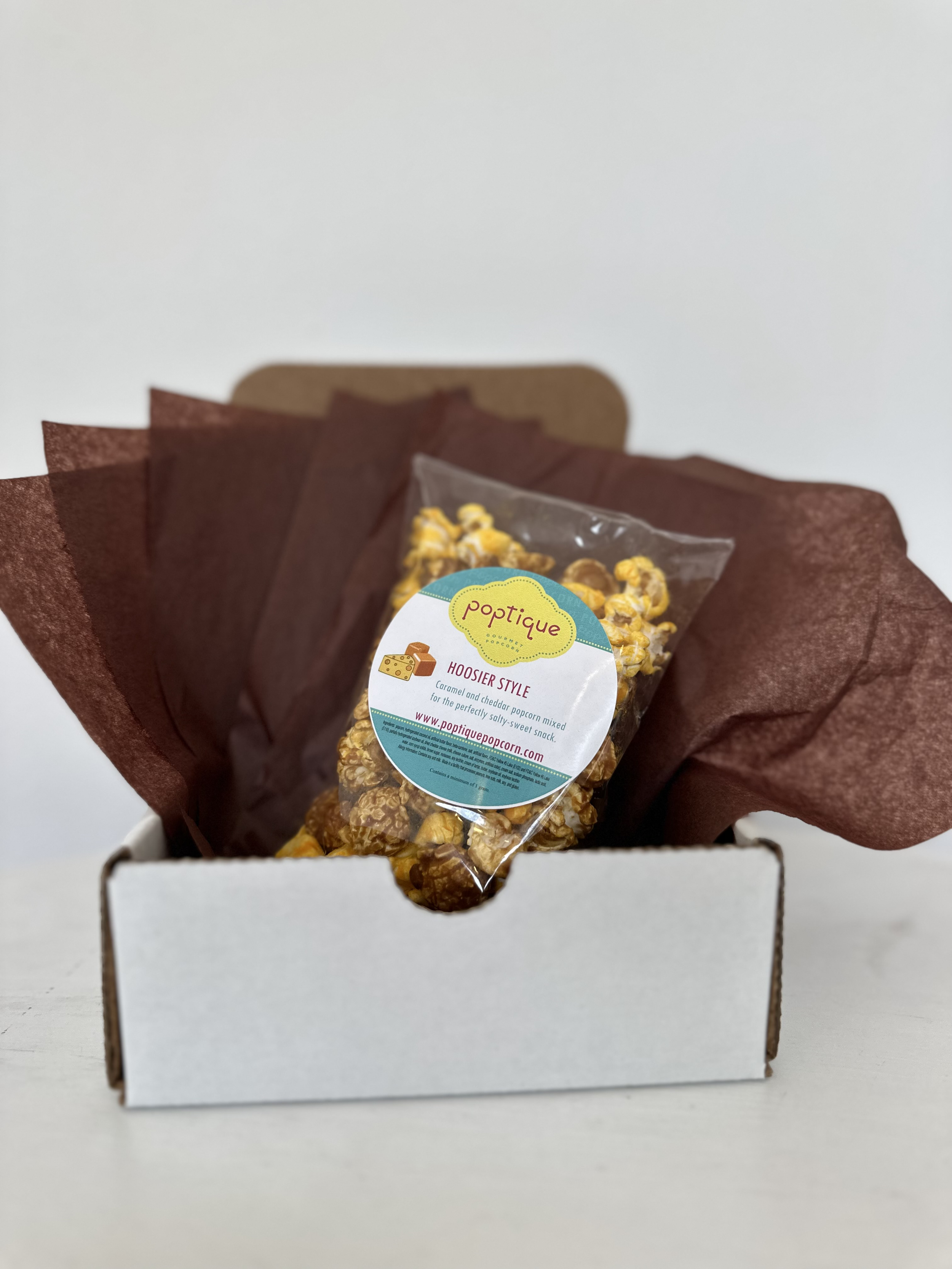 Bag of caramel and cheddar popcorn in a white box with brown tissue paper.