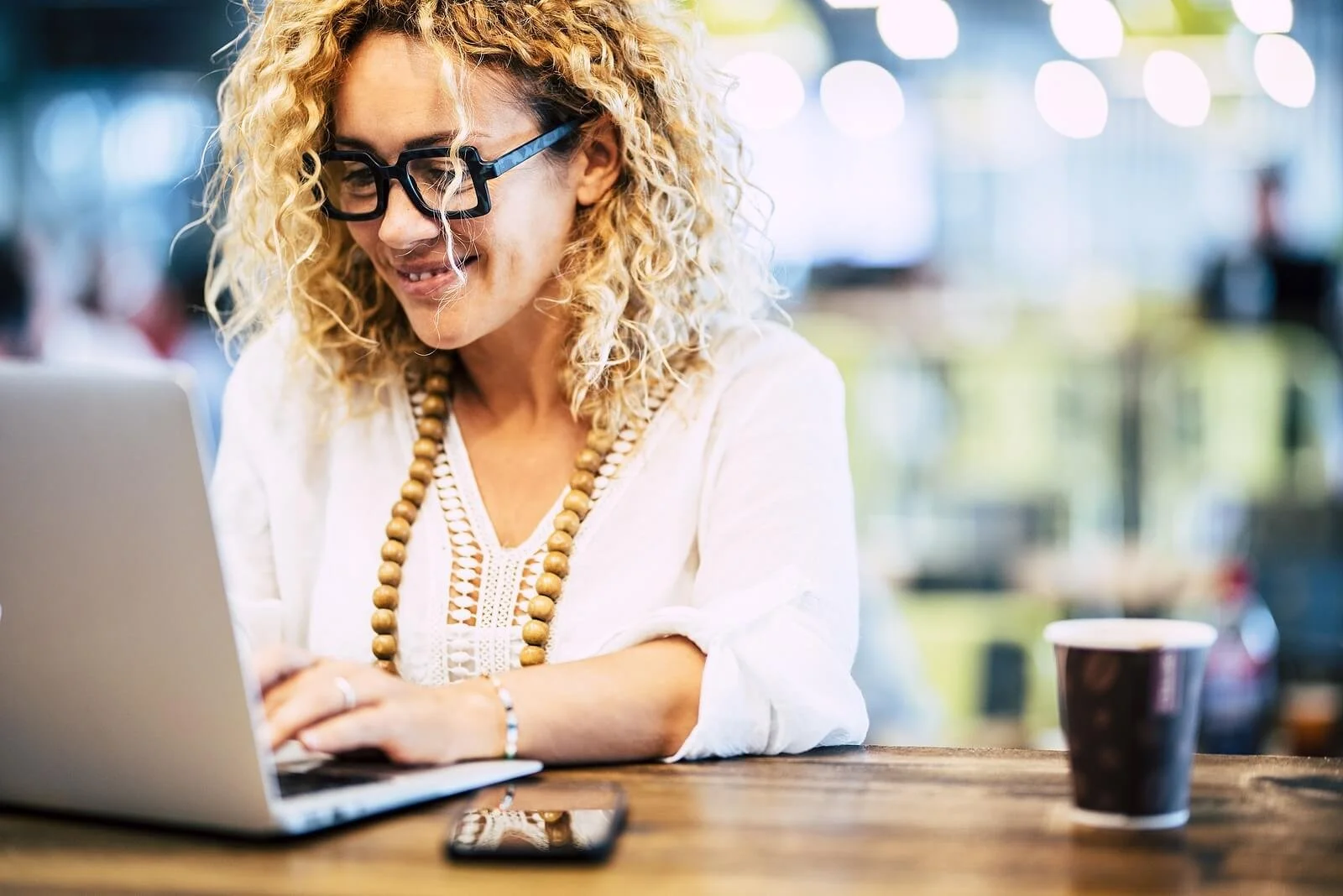Happy woman working on computer while sitting at a desk with a coffee cups near her.  Learn more about epresenting identity and self-worth therapy for women navigating midlife in Oakland and online throughout California.