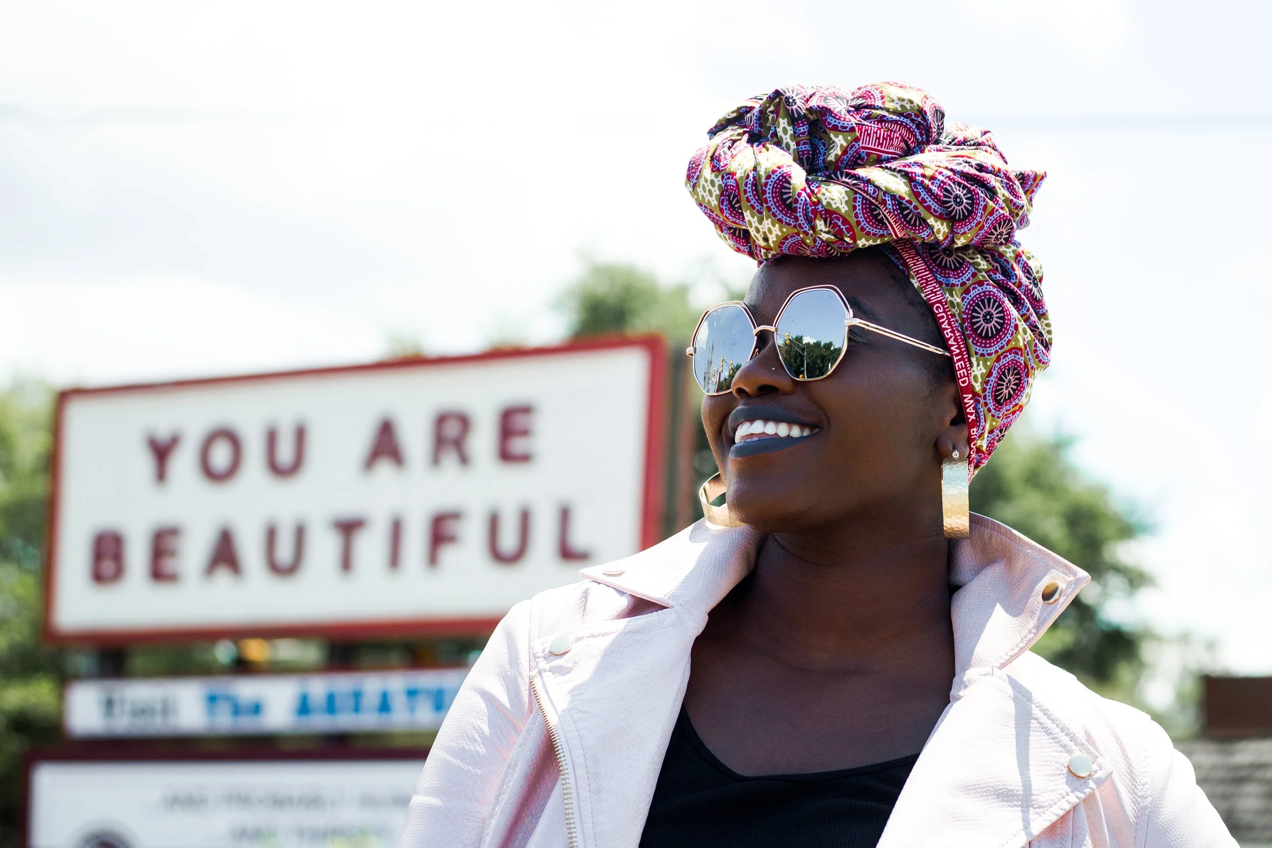 African American woman smiling in front of a sign that reads "you are beautiful.  This image symbolizing healing, self-discovery, and identity therapy for women in Oakland, the East Bay, and across California.