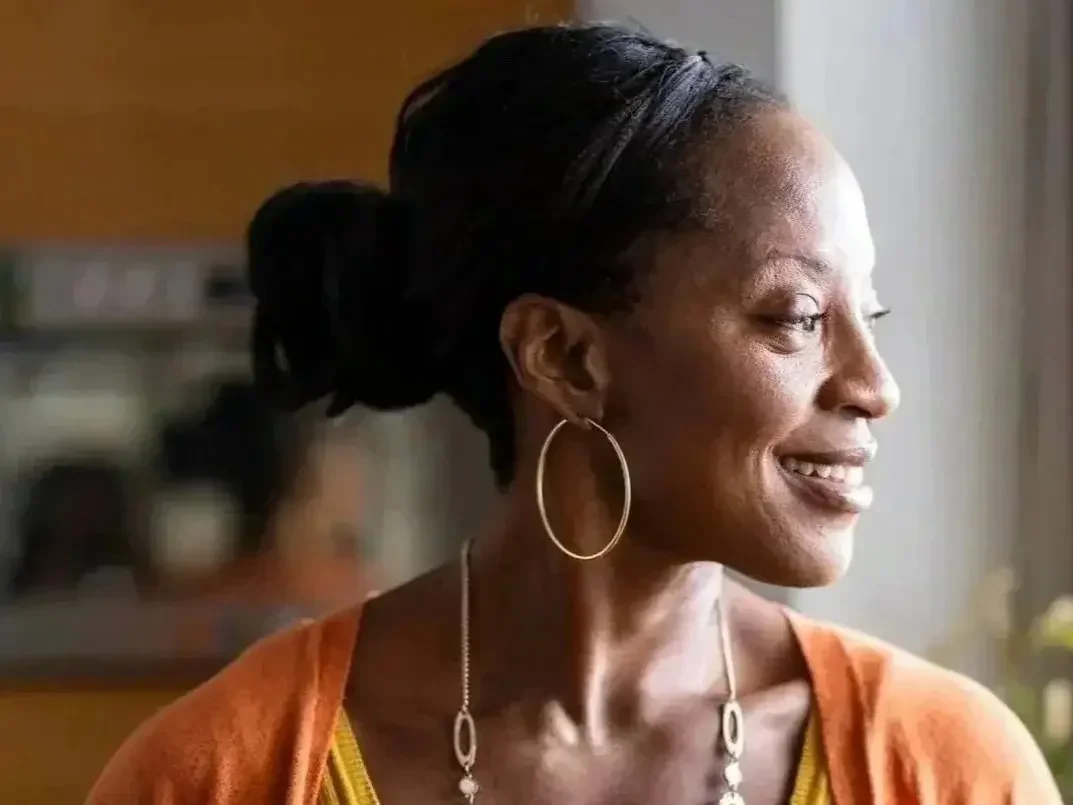 Middle-aged Black woman staring off into the distance smiling. This image represents the relief women can feel when they seek support for midlife transitions and perimenopause mood and anxiety.