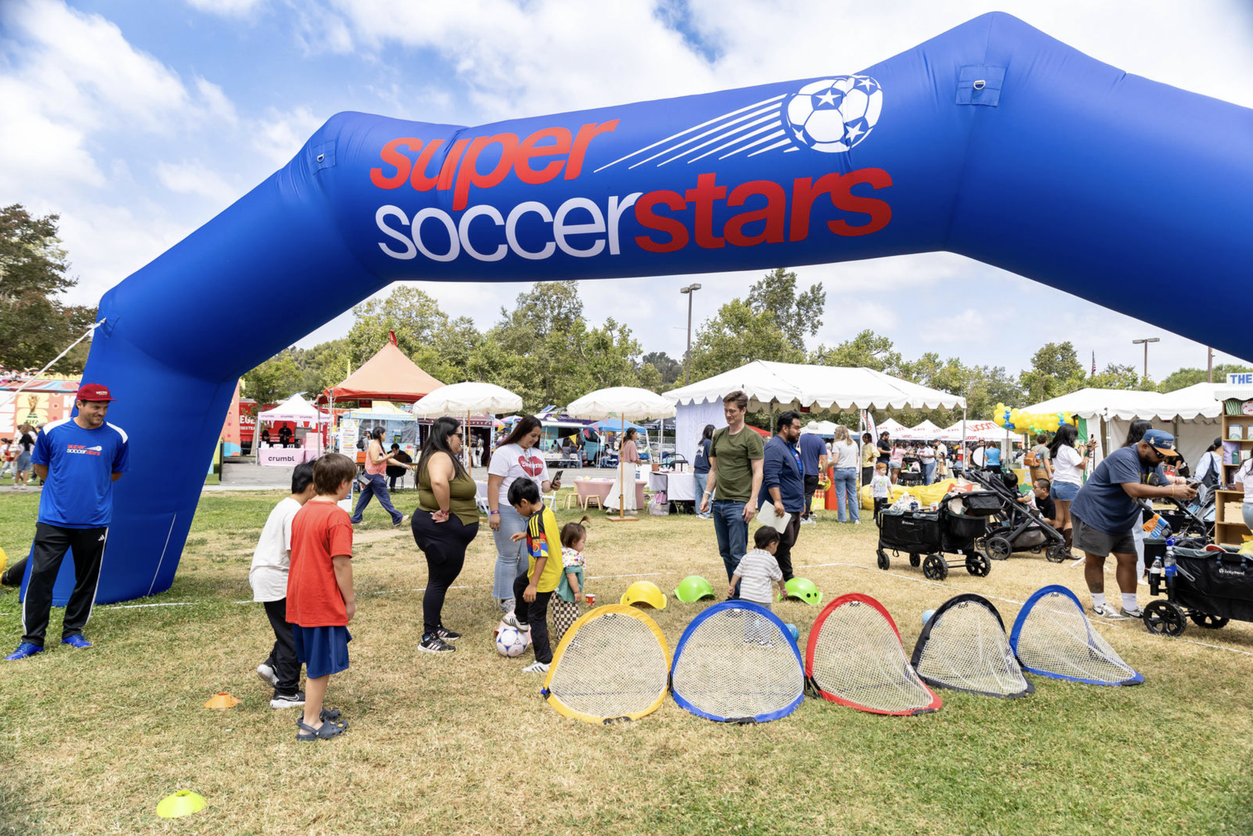 A young boy playing soccer on a grassy field surrounded by small red goals and soccer balls.