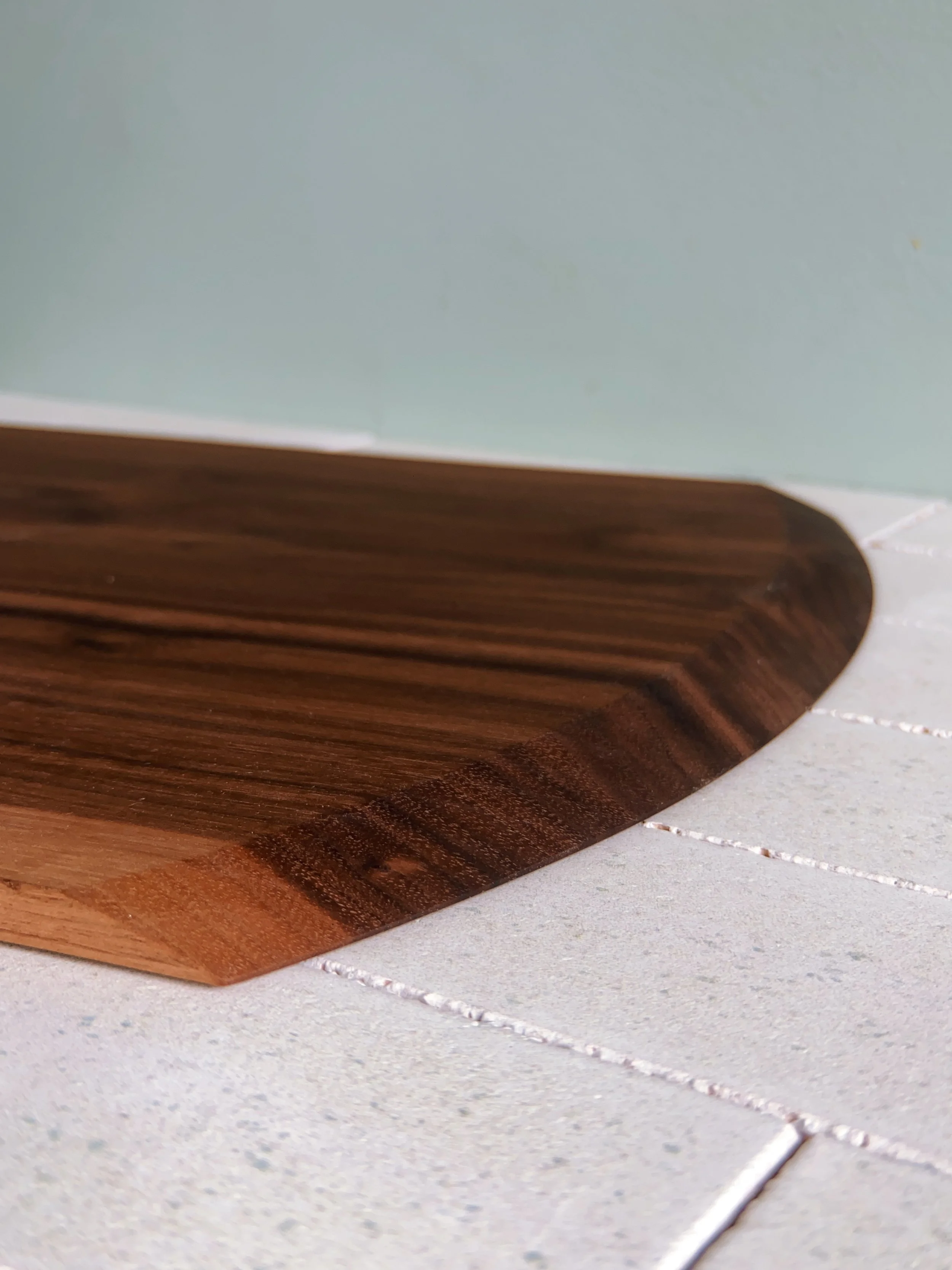 Close-up of a wooden pizza peel on a tiled countertop, with a mint green wall in the background.
