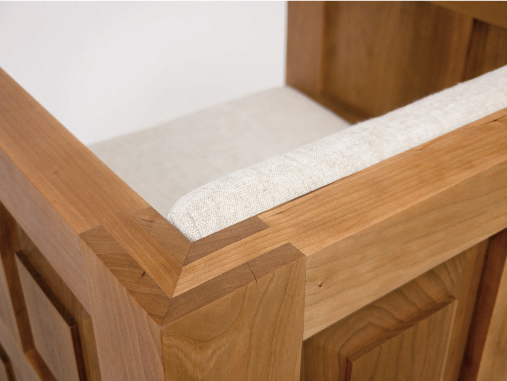 Close-up of a wooden club chair corner with a beige fabric cushion on top.