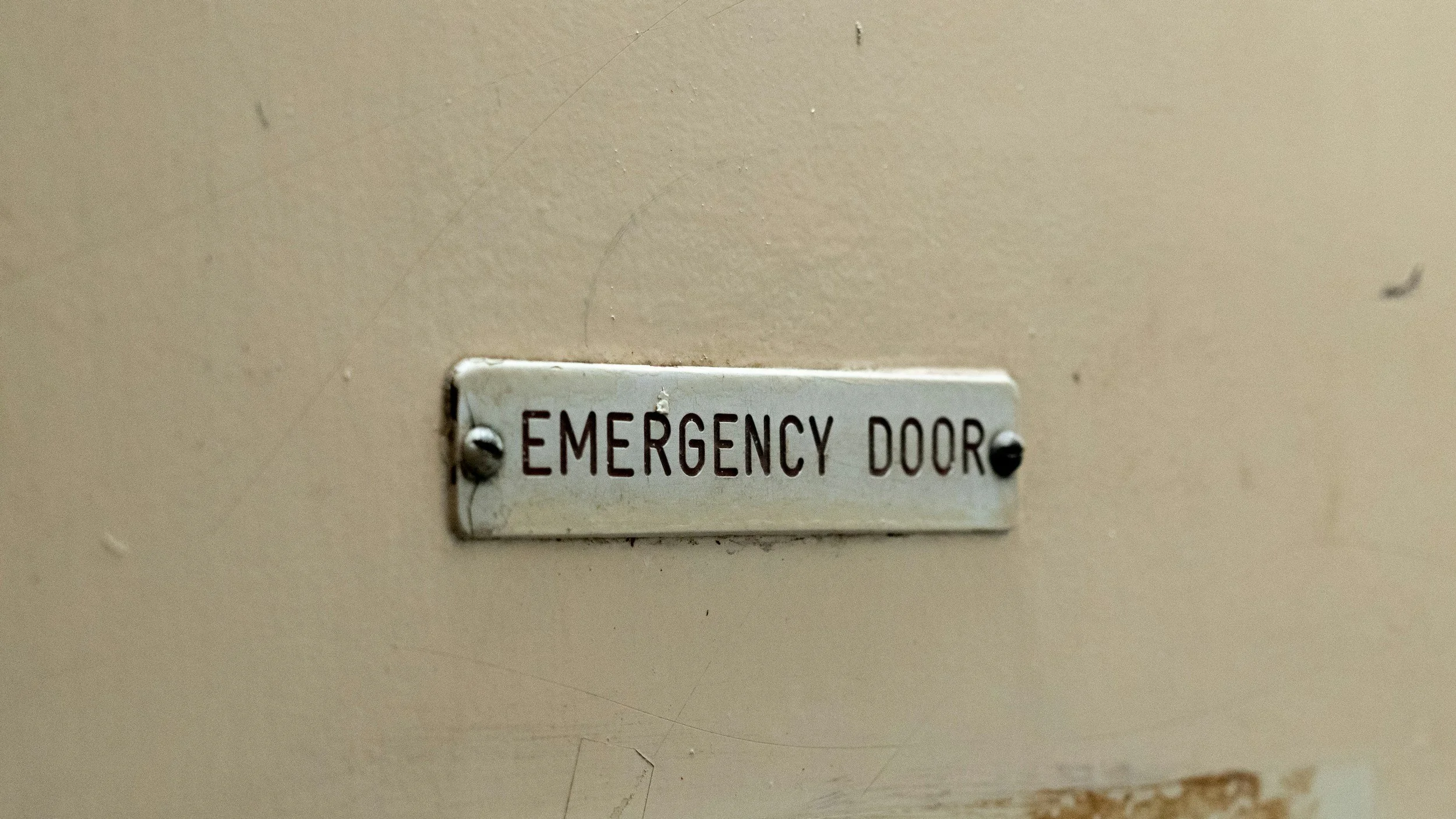 A metal plaque reading Emergency Door attached to a white scuffed background