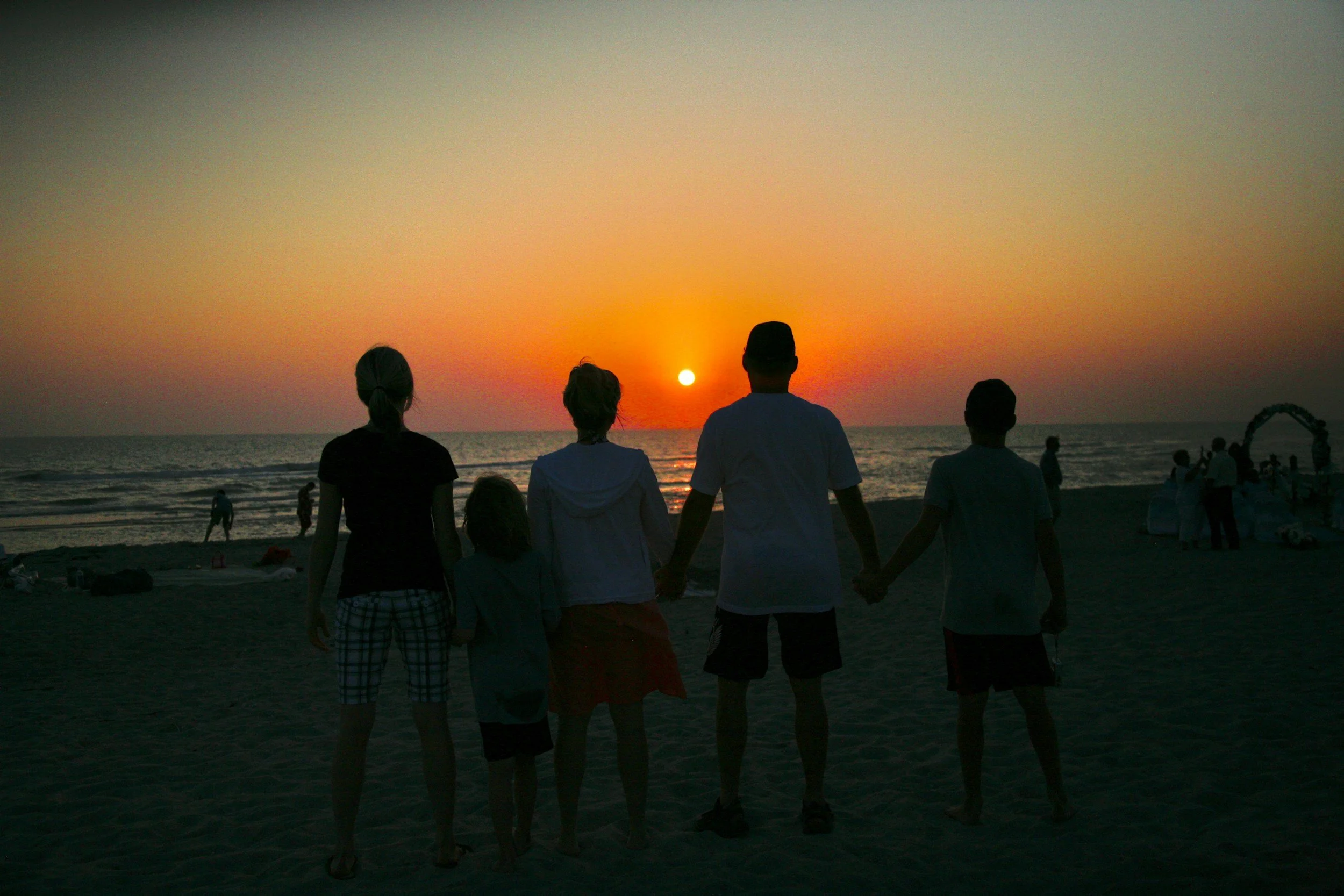 a group of people holding hands on the beach at sunset
