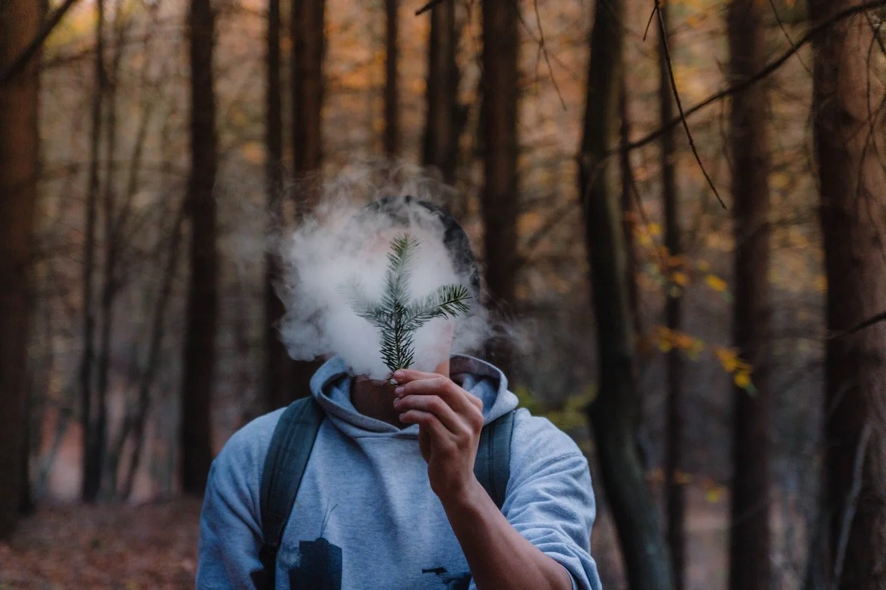 man blowing smoke on a branch