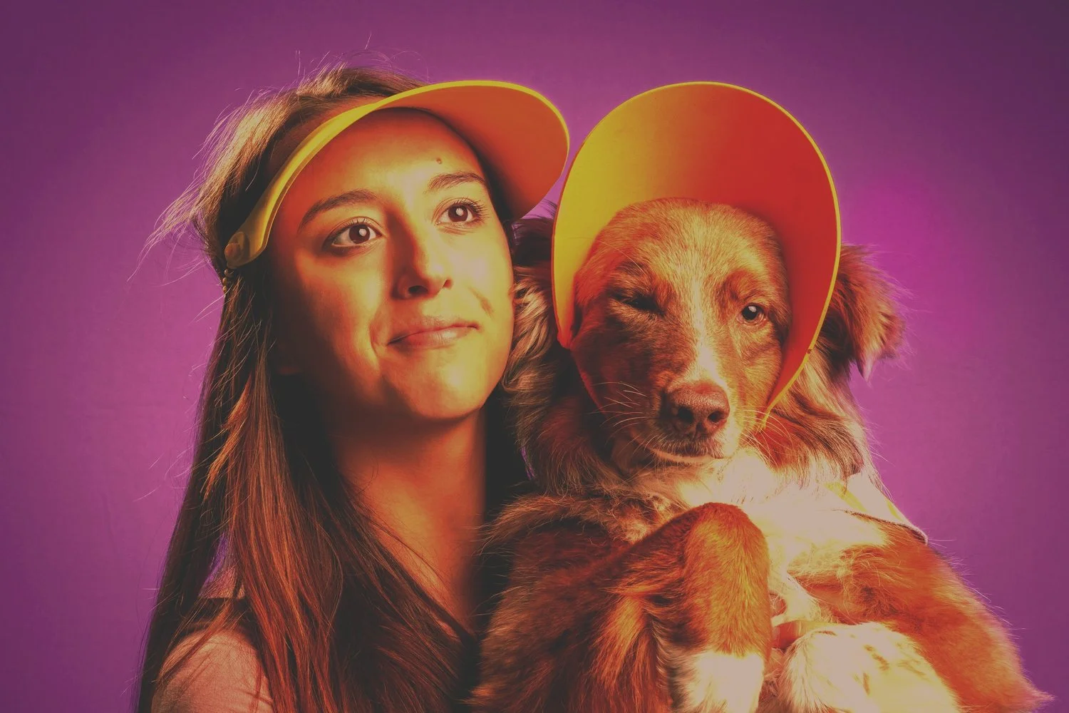 A young woman and a dog wearing yellow visors against a purple background.