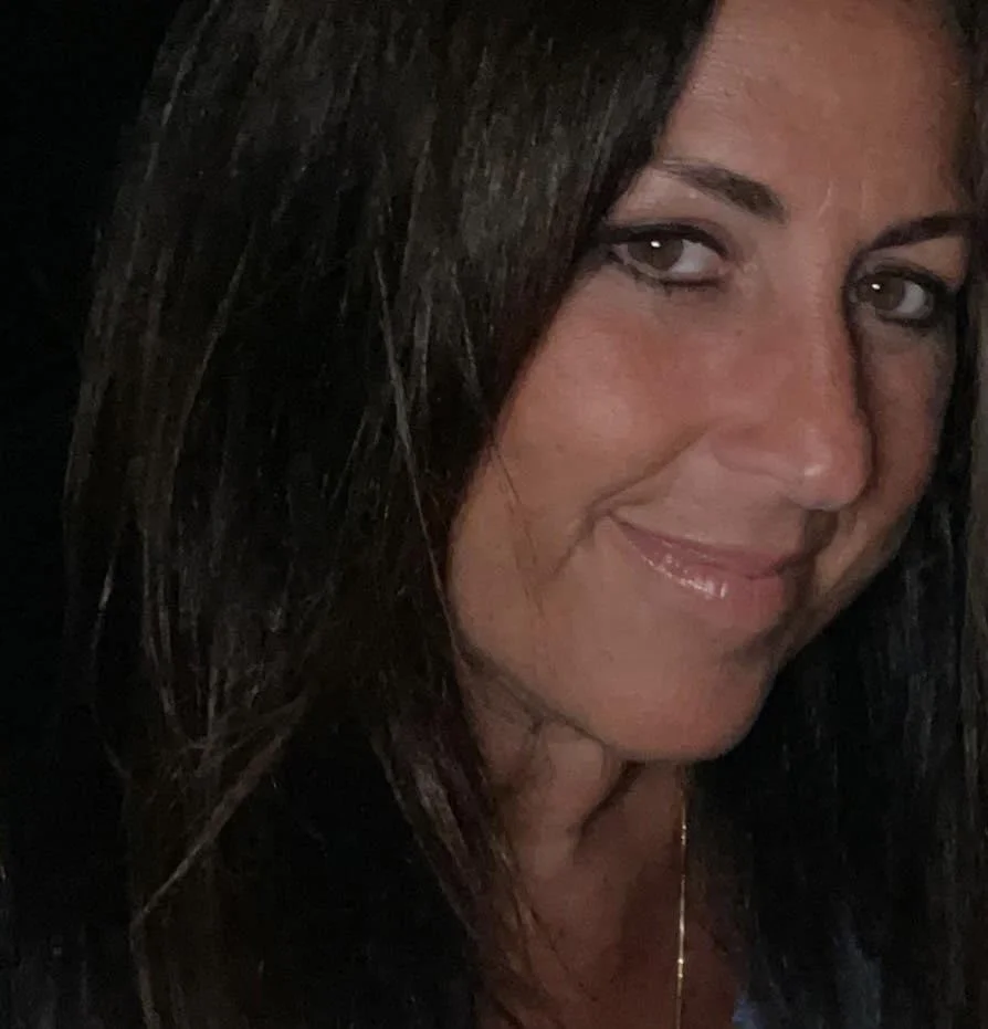 Close-up of a woman with long dark hair smiling slightly, against a dark background.