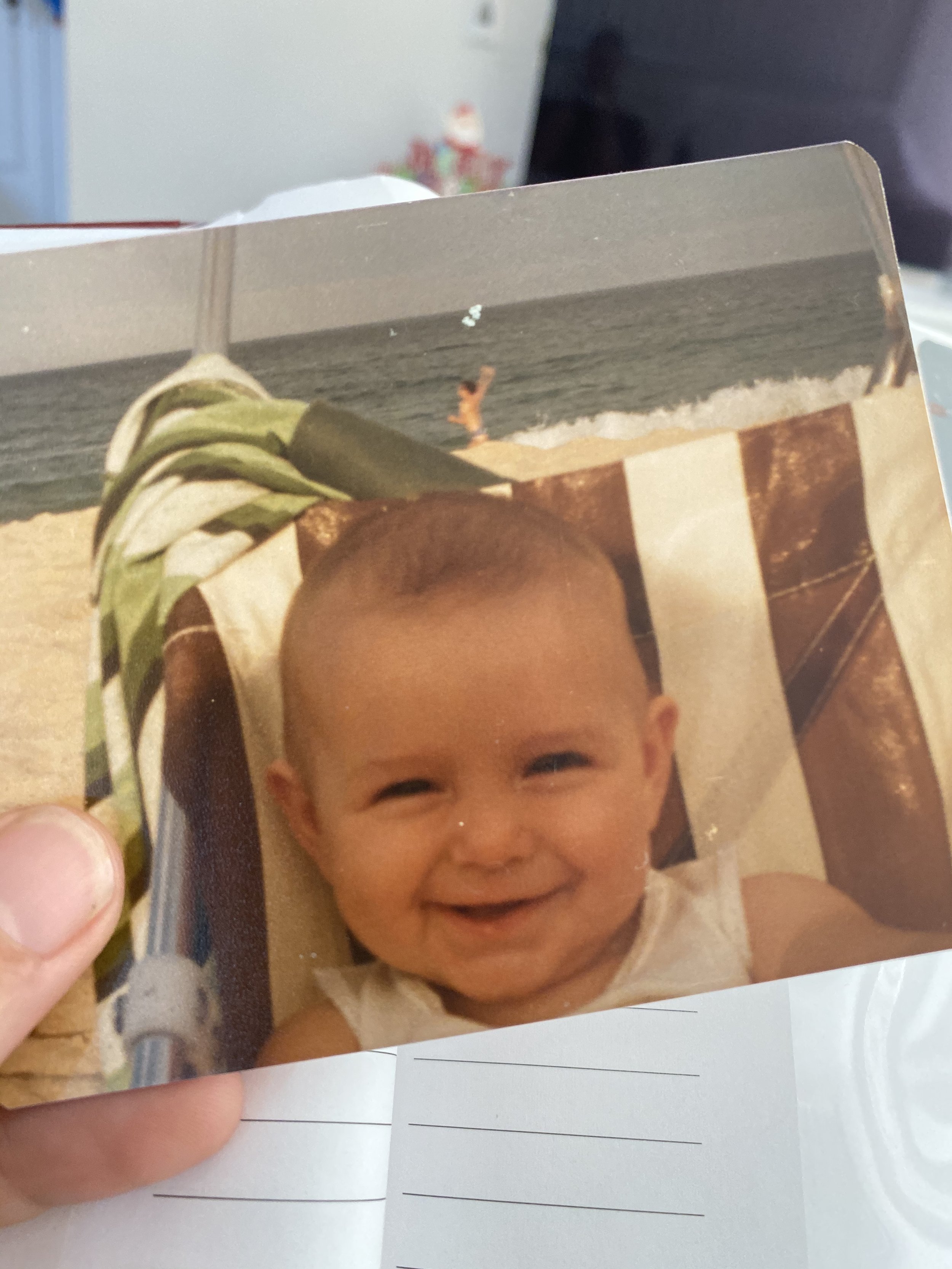 A smiling baby Nicole in a stroller on a beach with the ocean in the background.