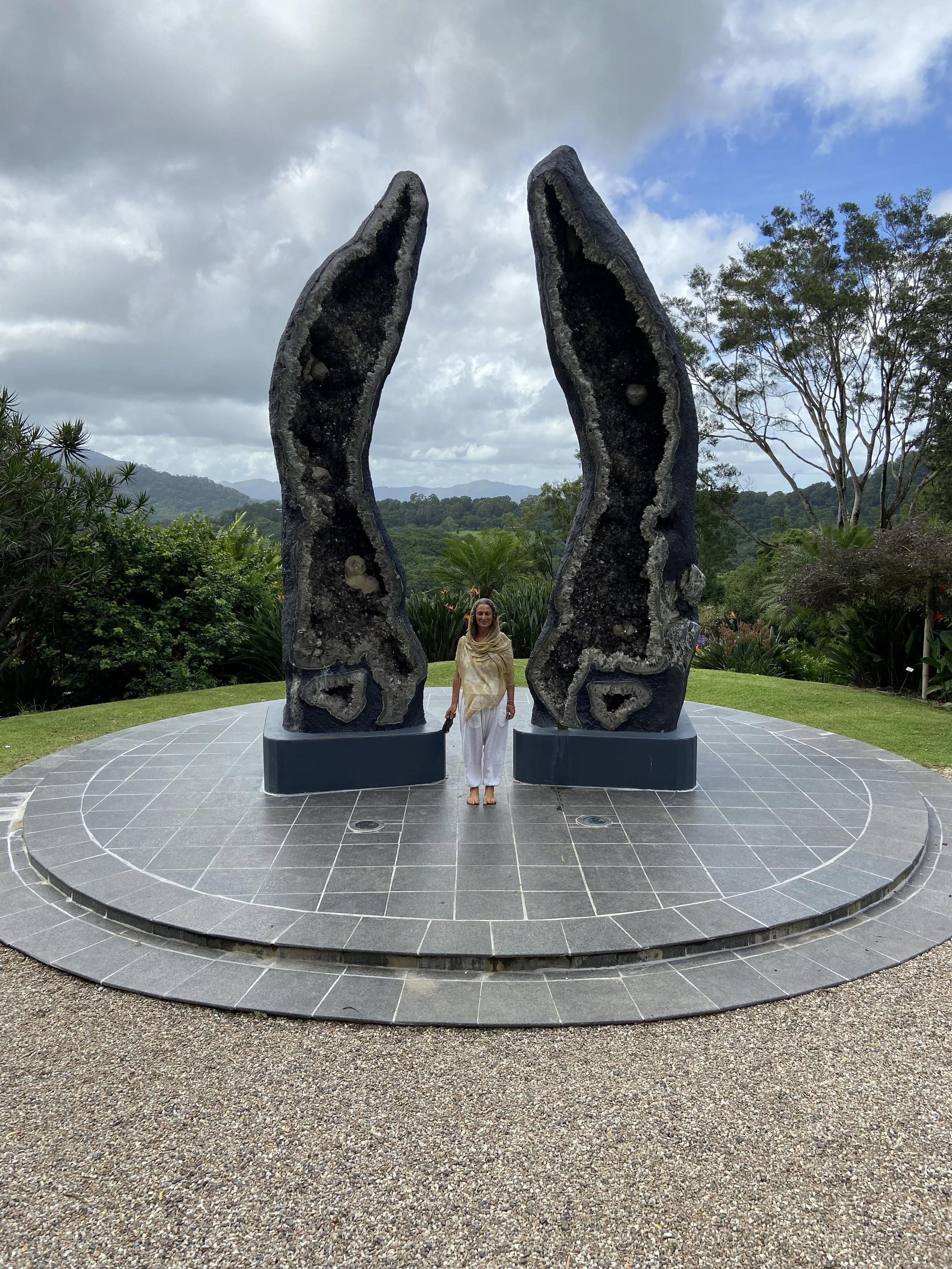 Nicole standing between two large geode sculptures on a tiled platform with a scenic natural background.