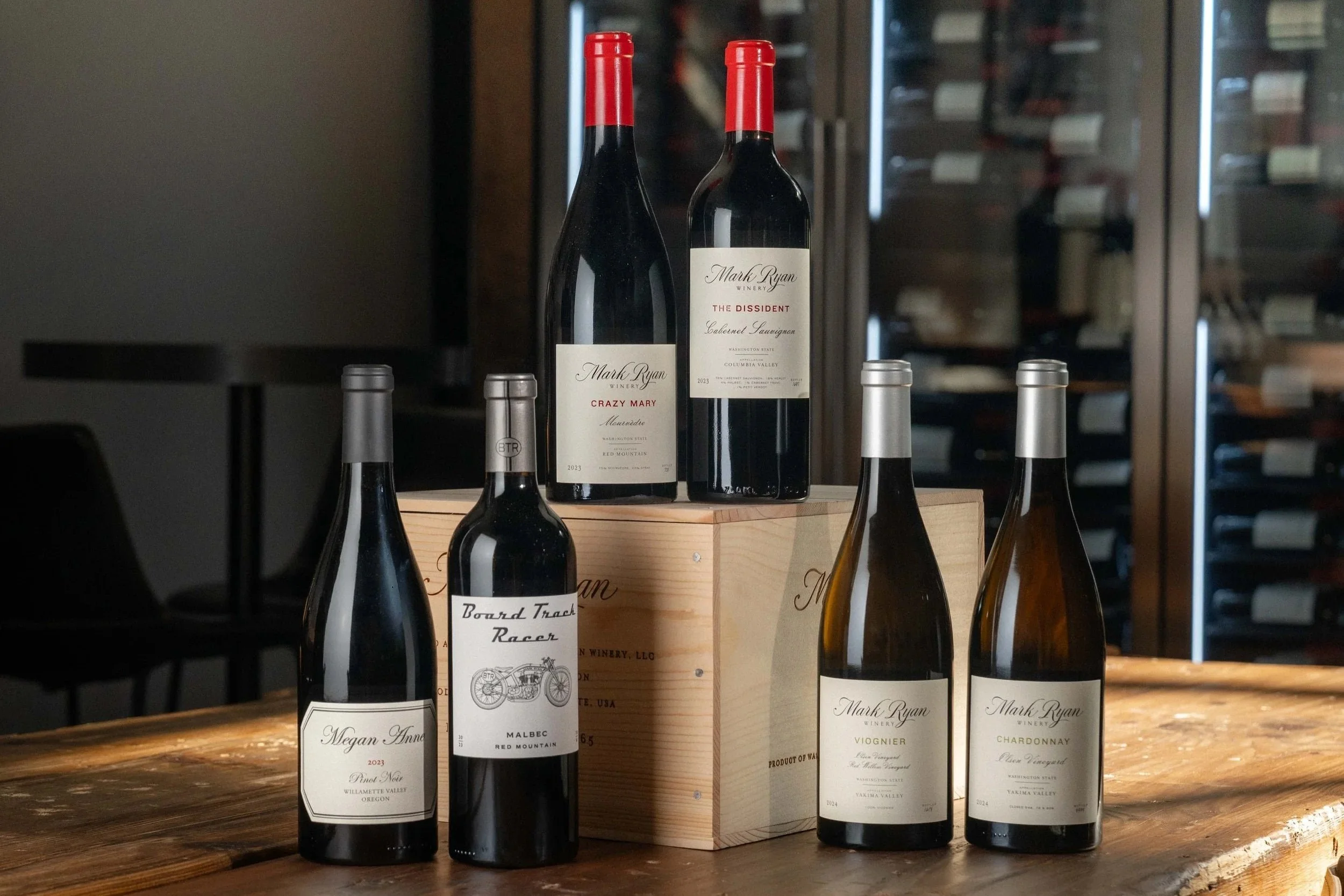 Six wine bottles from the Crowd Pleaser Series from Mark Ryan Winery displayed on an elegant wood table.