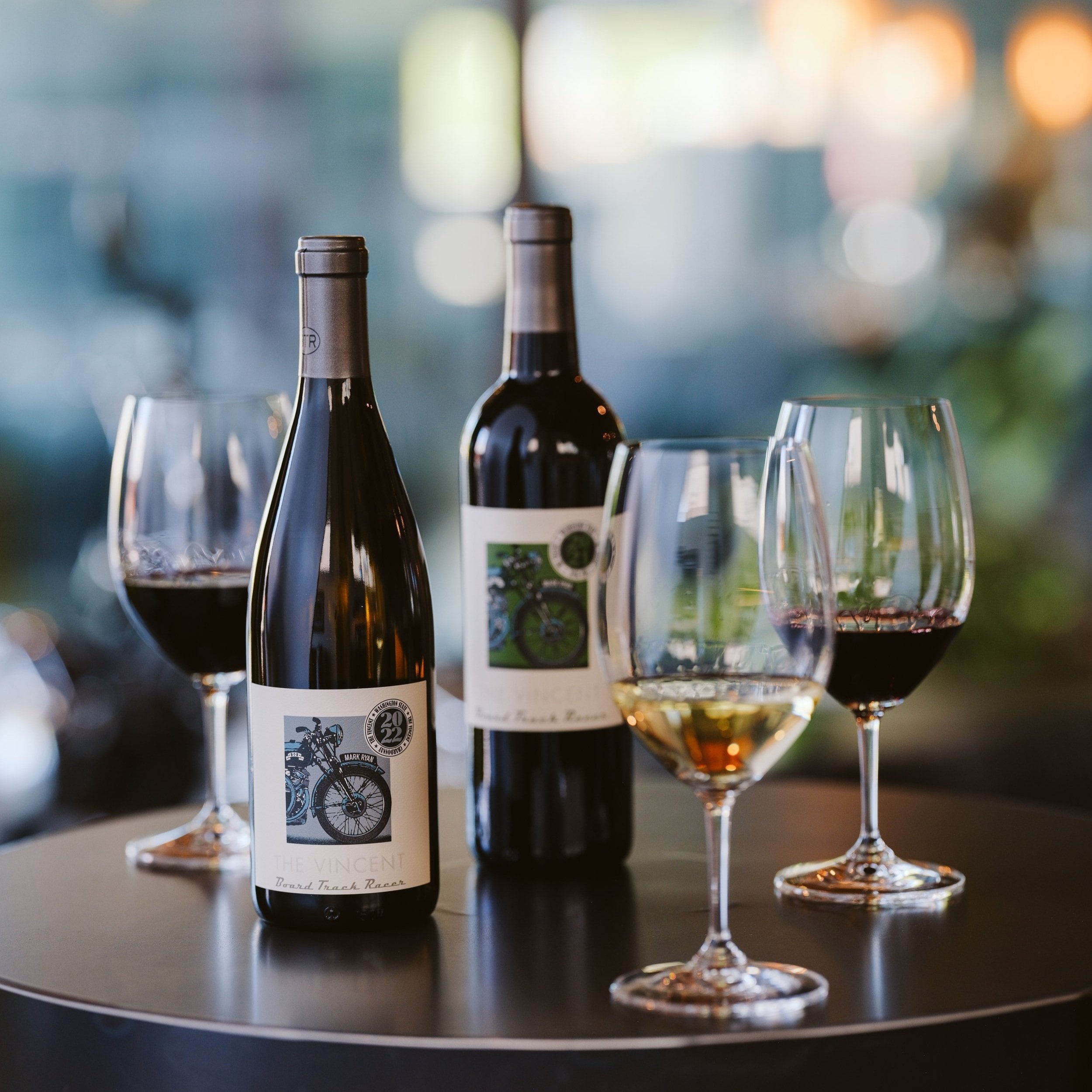 Two bottles of wine from Board Track Racer on a concrete table surrounded by full glasses of wine.