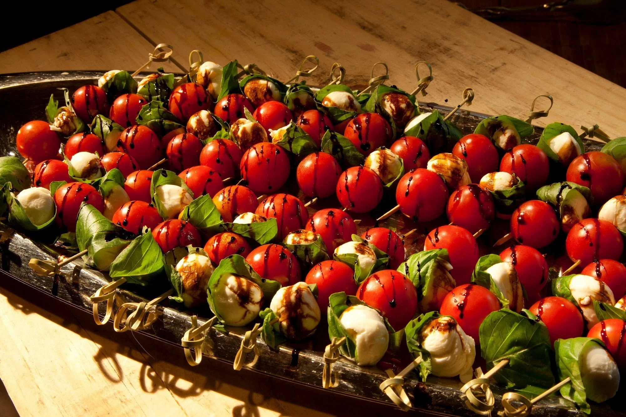 Caprese skewers drizzled with balsamic vinegar arranged neatly on a platter.