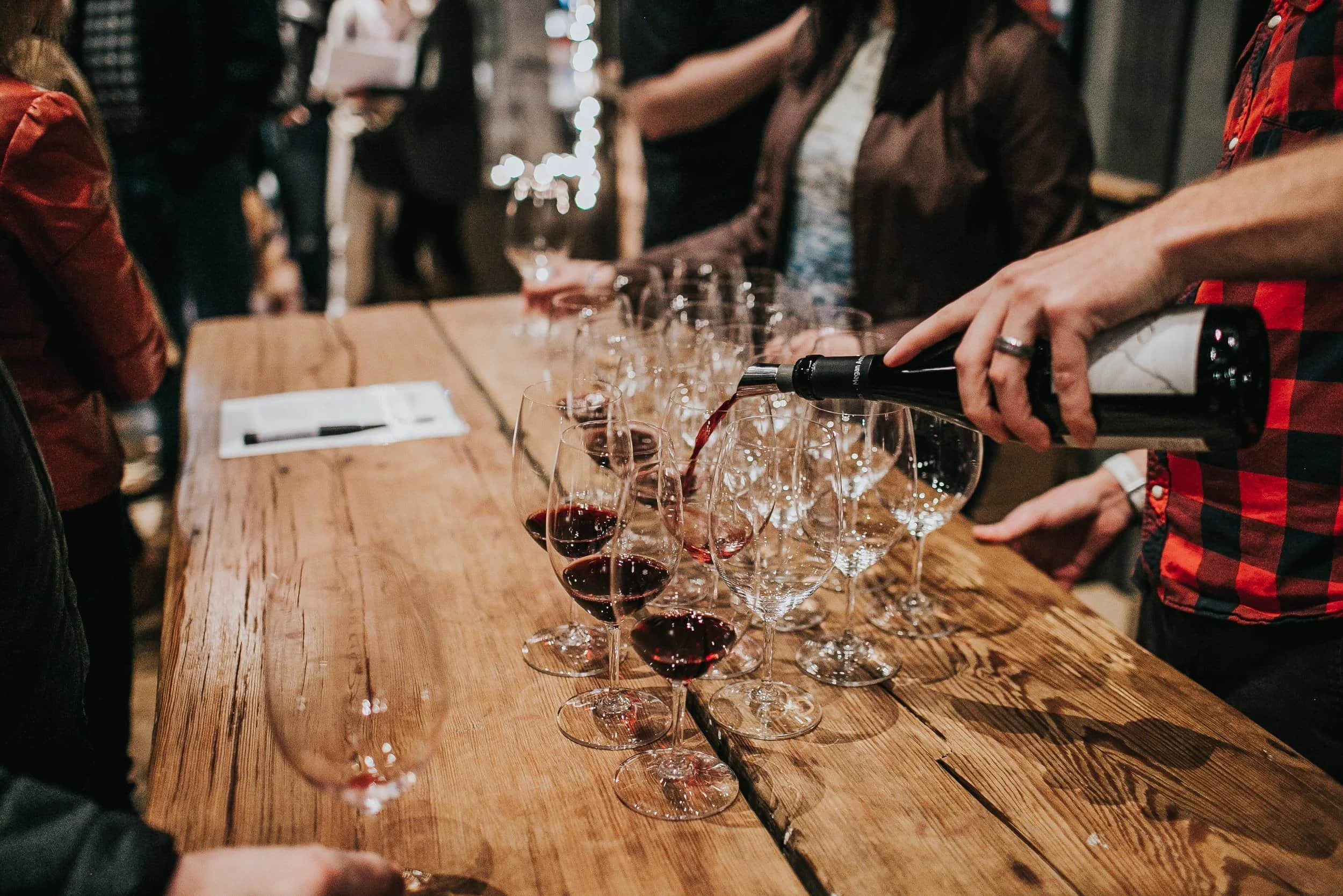 Wine pouring into multiple glasses lined up on an elegant wooden table.