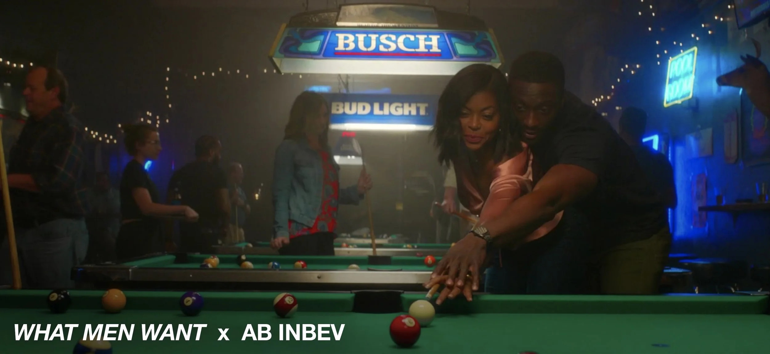 A man and woman playing pool in a dimly lit bar, with a group of people in the background and neon signs on the wall.