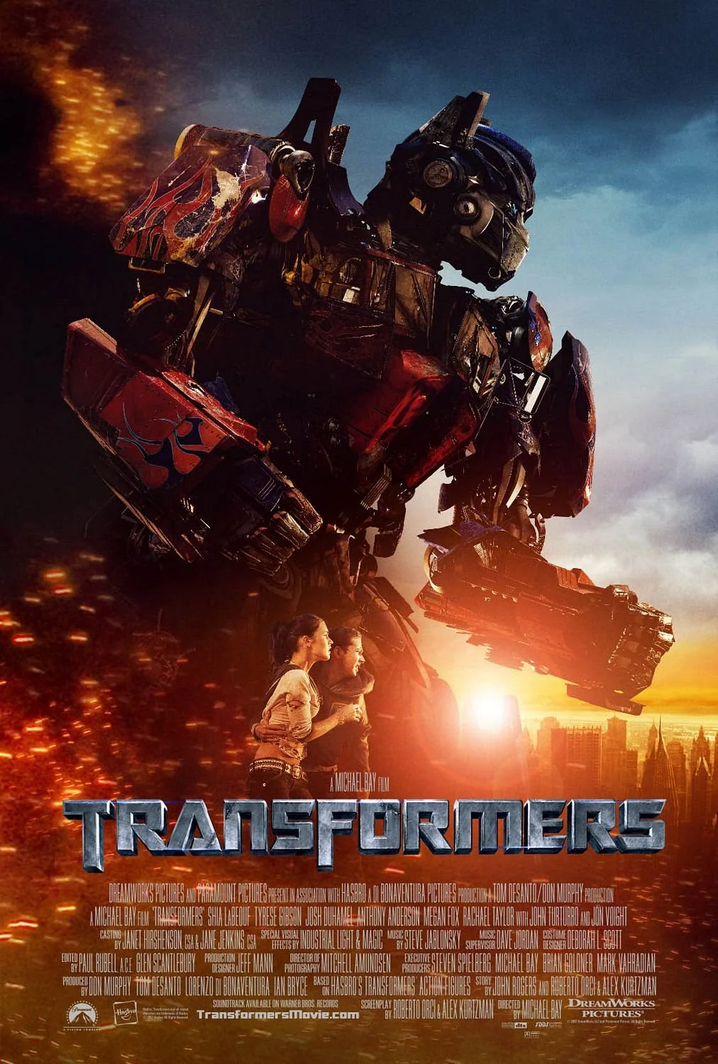 Movie poster for Transformers featuring Optimus Prime in a cityscape at sunset with two women, and the title 'Transformers' at the bottom.