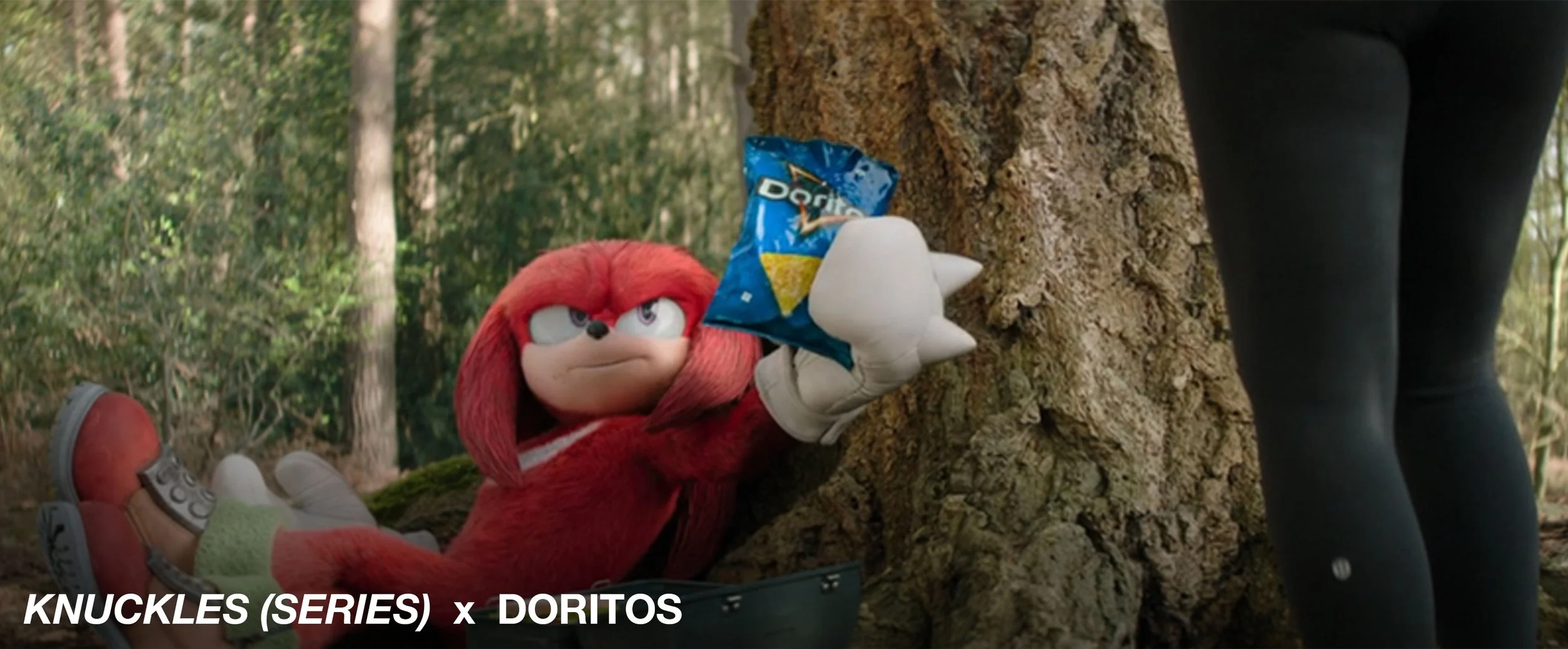 Knuckles the Echidna from Sonic the Hedgehog lying on the ground holding a bag of Doritos in his right hand, with a serious expression, in a forest setting. Part of a person's legs in black leggings is visible on the right.