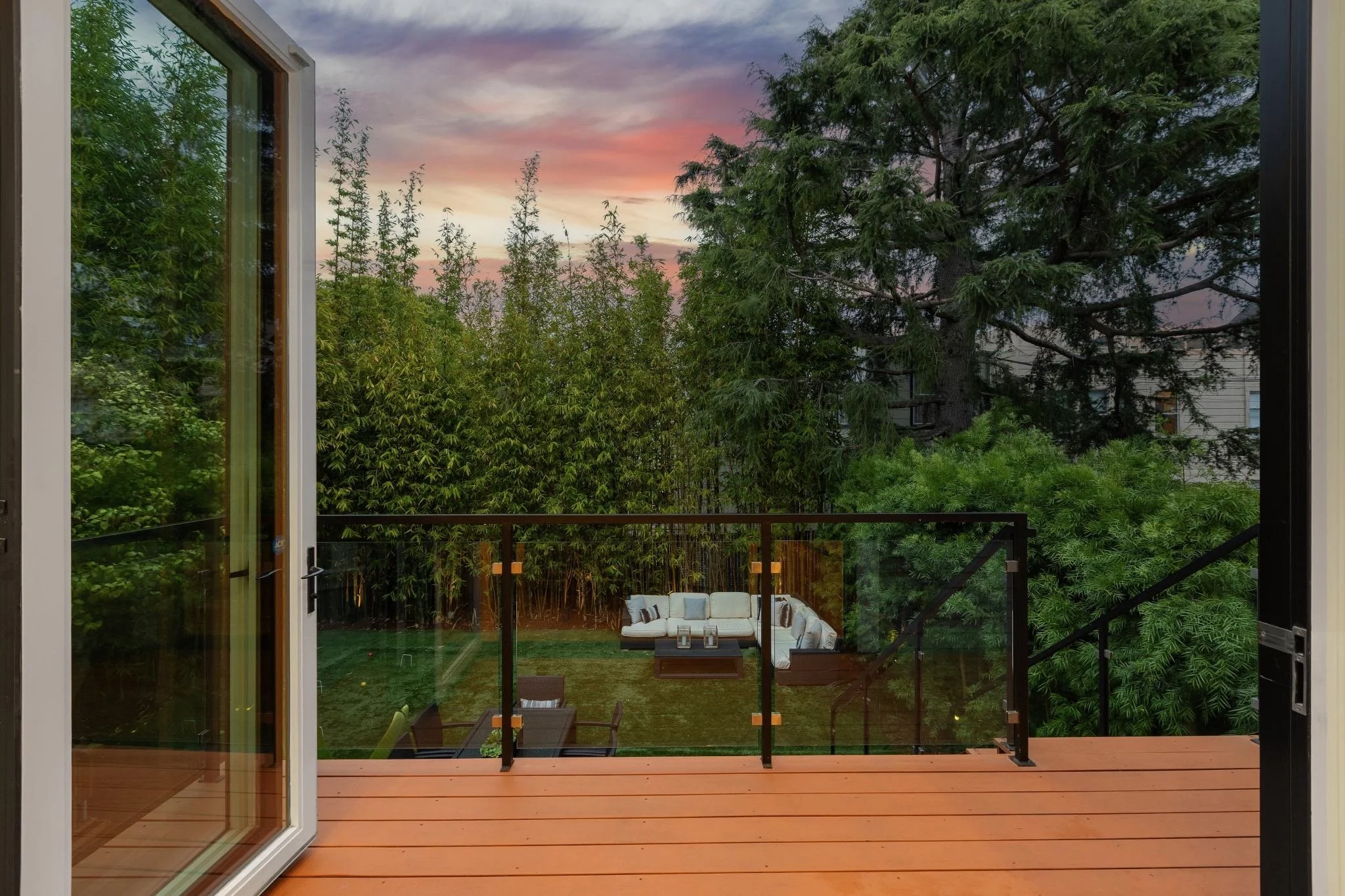 View from a patio looking into a backyard with outdoor furniture, lush trees, and a colorful sunset sky.