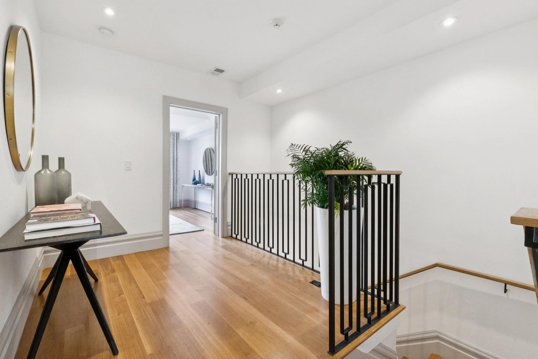 Interior view of a home with white walls, hardwood floors, a black metal staircase, and a green potted plant near the staircase.