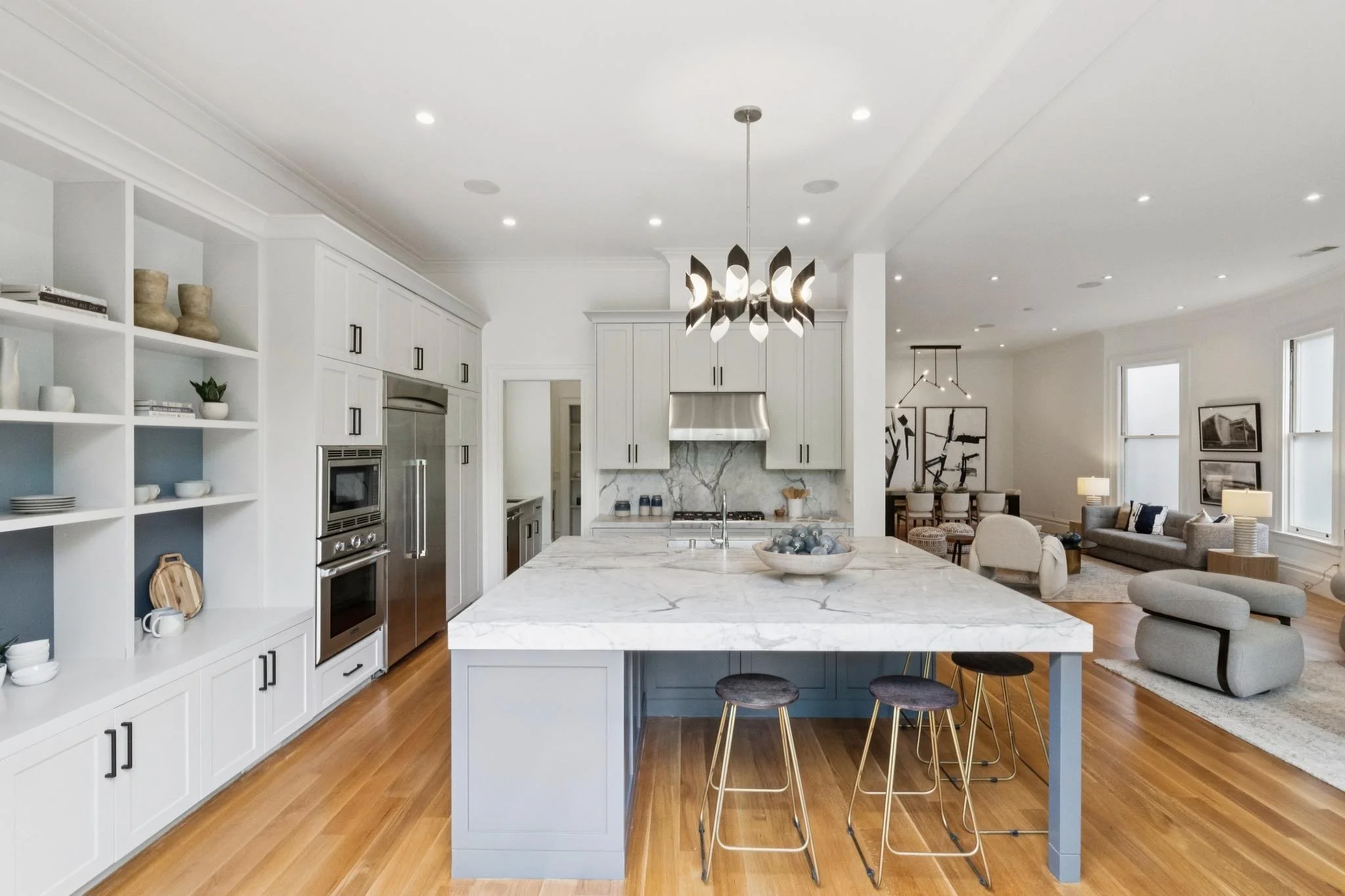 Modern open-concept kitchen and living area with white cabinetry, marble island, pendant lighting, and a sitting area with sofas and artwork.
