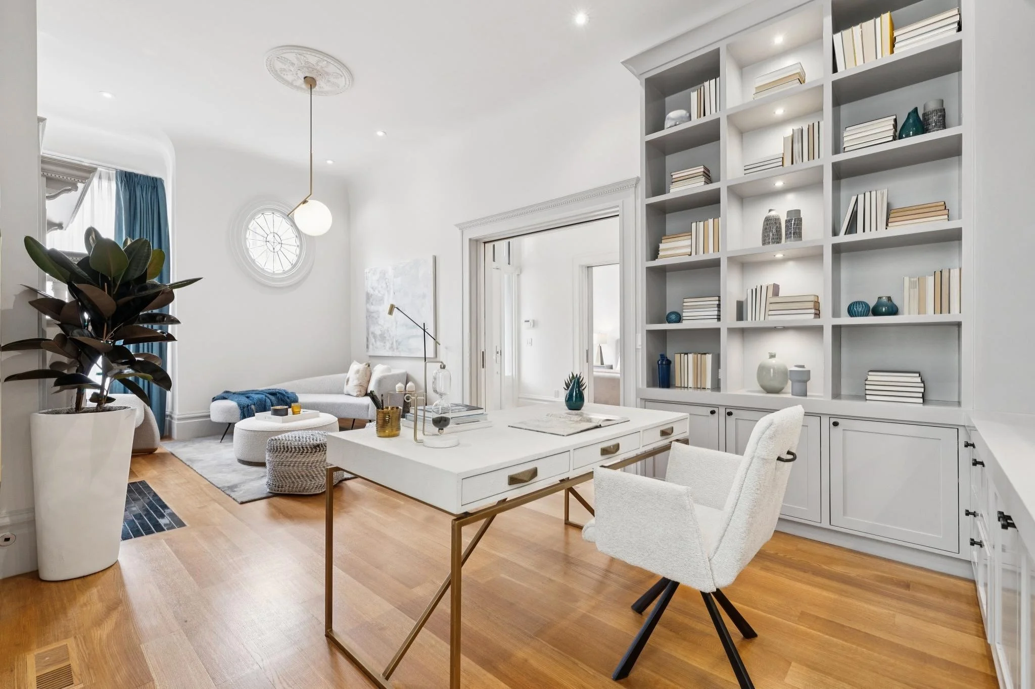 A bright, modern living space with white walls and furniture, a large built-in bookshelf with decorative items, a white couch, and a wooden floor.